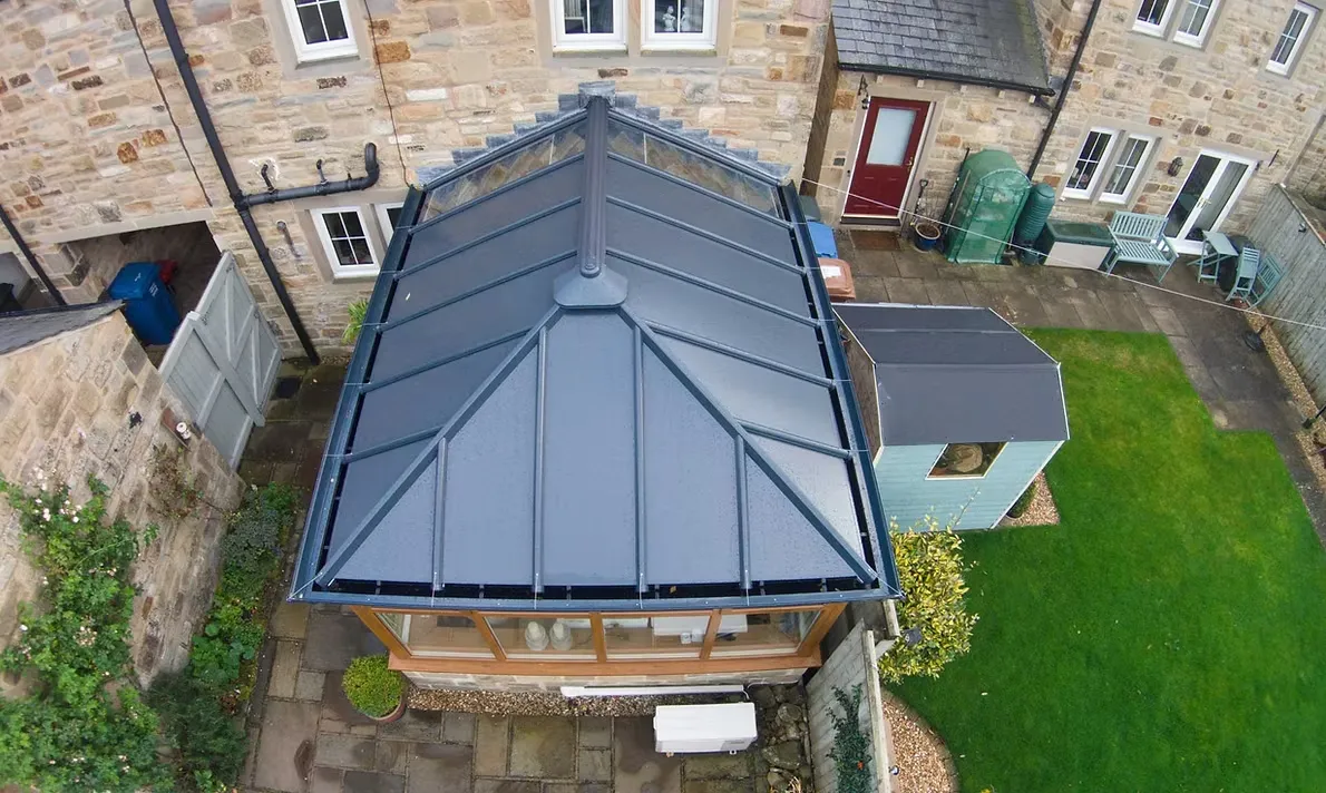 Aerial view of a grey tiled warm conservatory roof replacement on a traditional stone house.