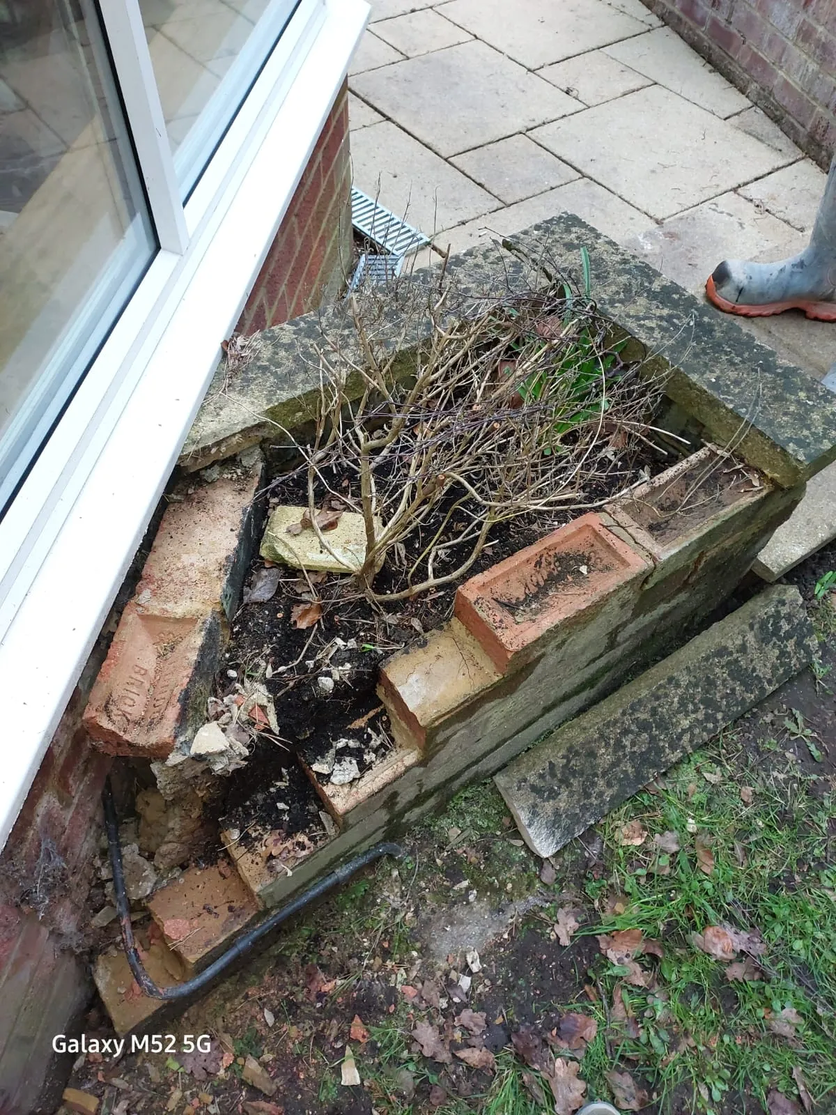 Close-up of an ACO channel drain in a paved area, with nearby brickwork being repaired or excavated for drainage work.