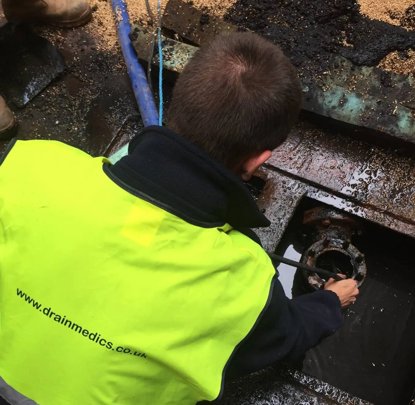 A Drain Medics technician attending to a drain problem, with the company website visible on their high-visibility vest.