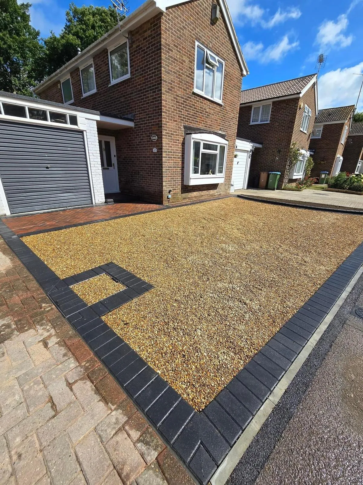 Newly laid gravel driveway with dark block paving edge and integrated drain in front of a modern brick house.