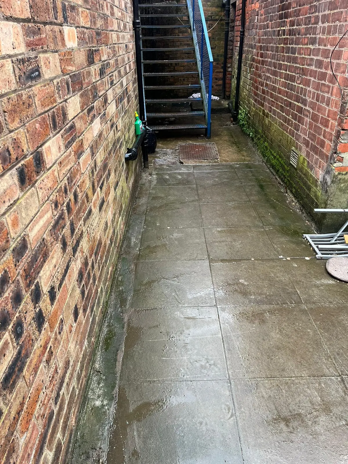 Standing water on a paved area next to a wall, indicating a potential drainage problem.