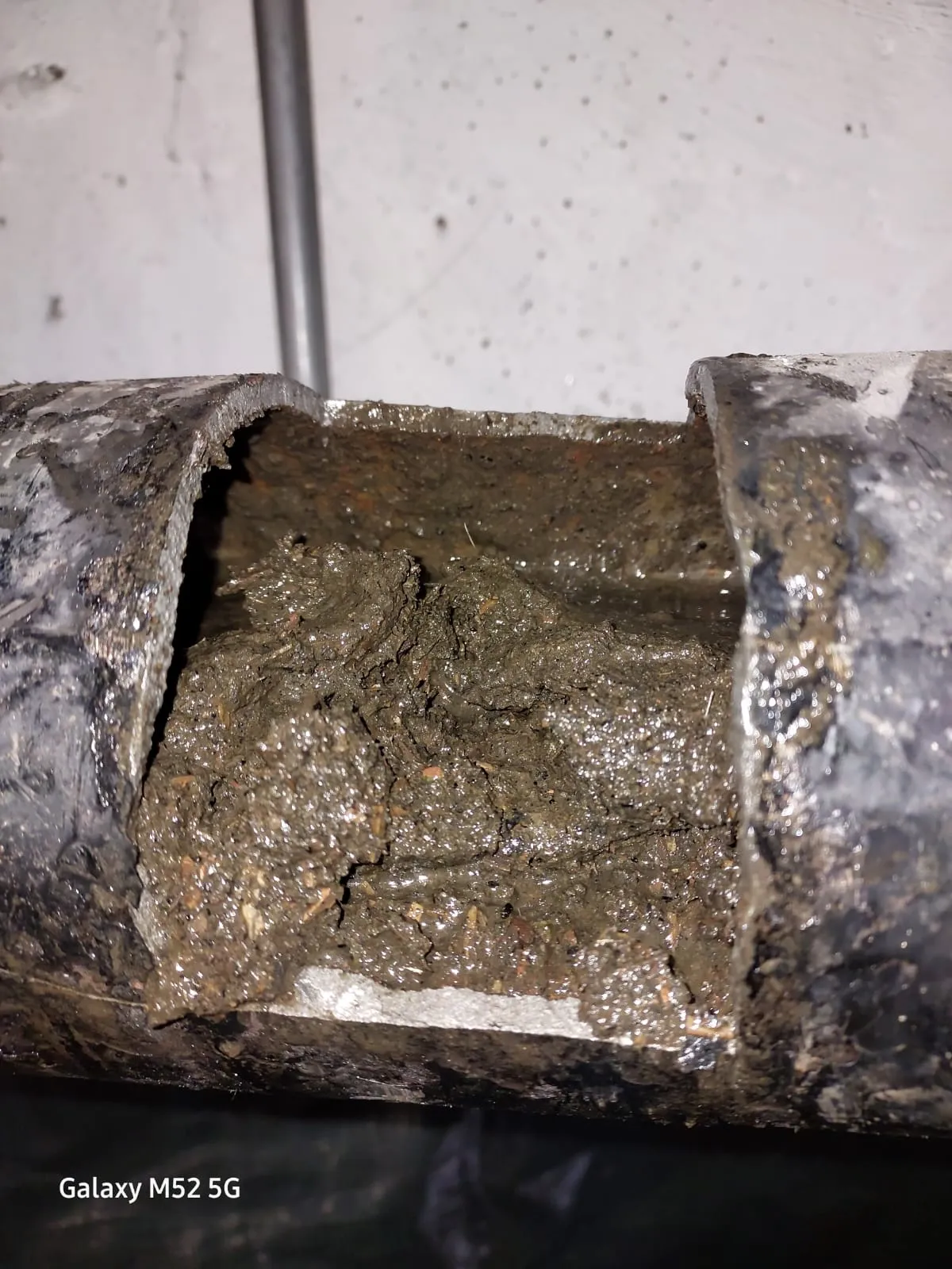 Close-up of a cut-open drain pipe showing a heavy blockage of sludge, dirt, and debris inside.