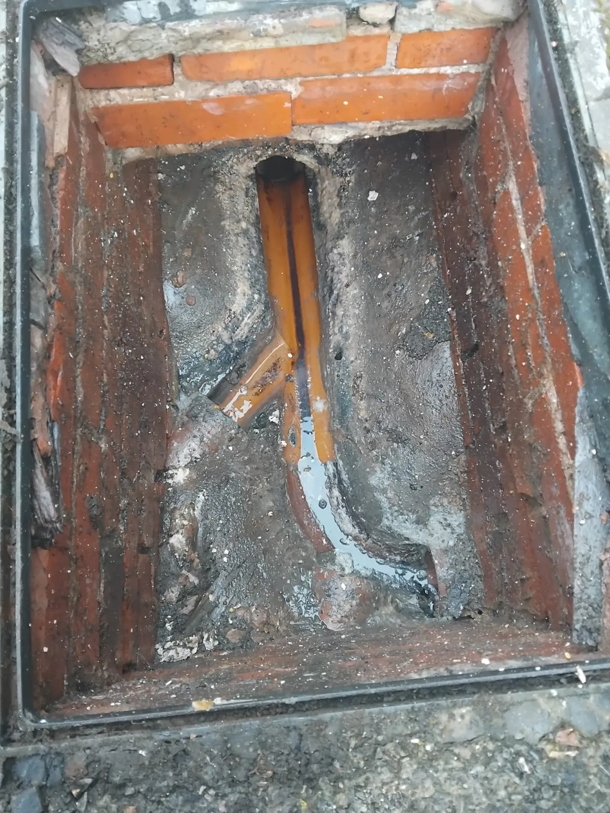 An open drain inspection chamber with standing dirty water and pipework.