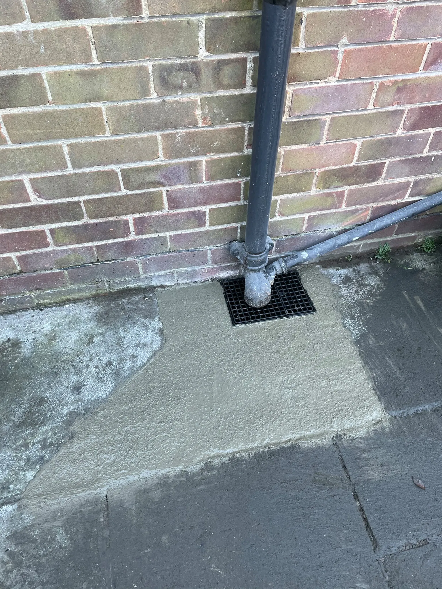 Newly installed drain gully next to a brick wall with neat concrete surroundings
