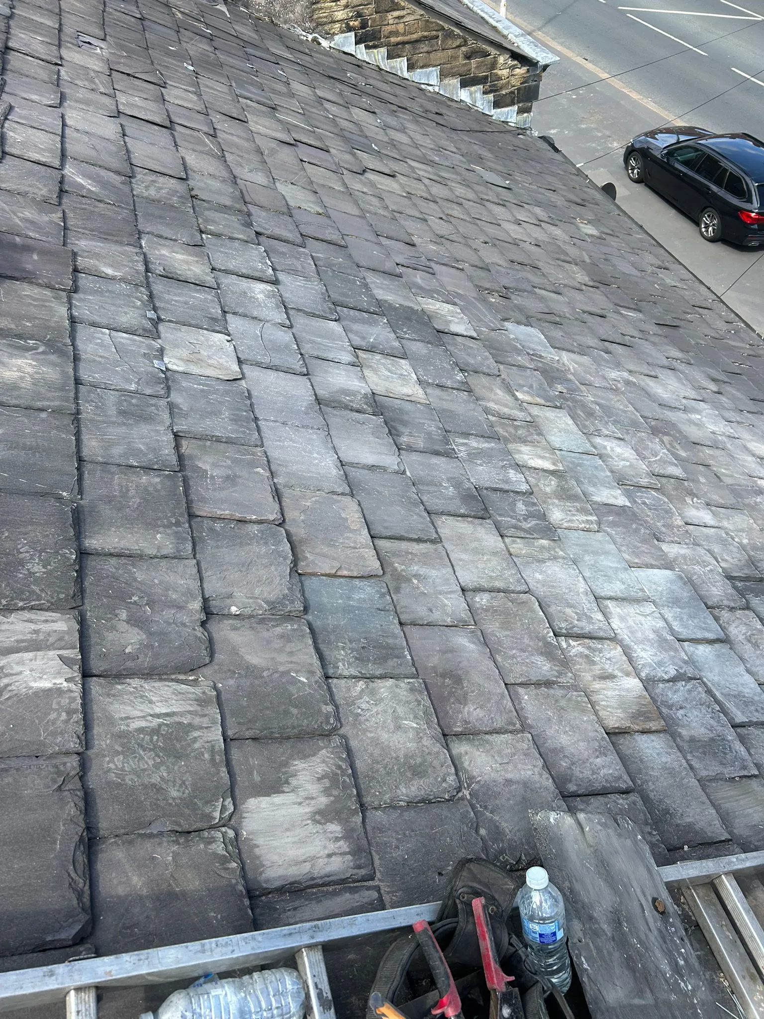 Old grey slate roof with a ladder and tools during a repair or inspection.