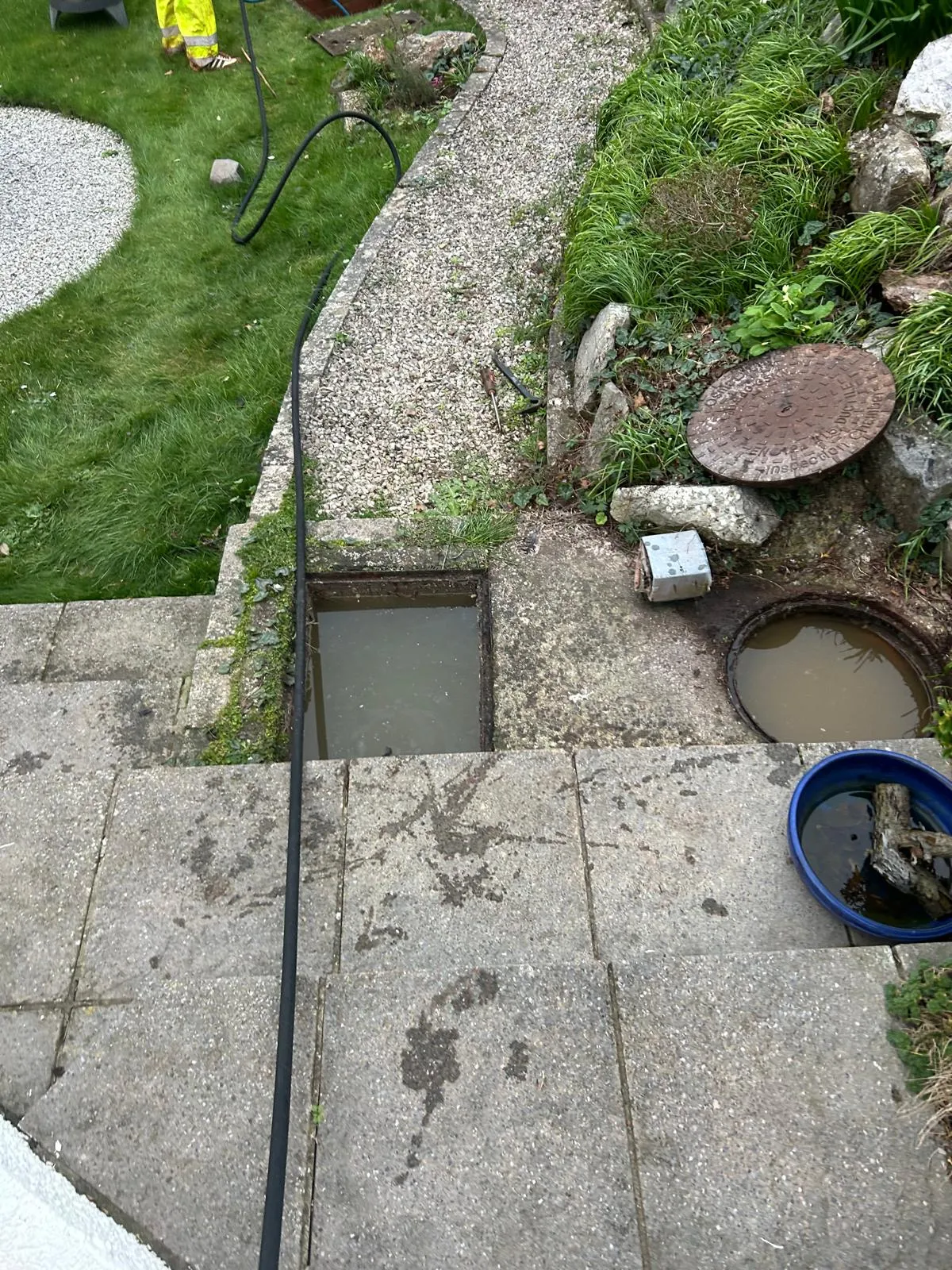Drainage engineer using a high-pressure jetting hose to unblock an overflowing external drain or manhole at a property.