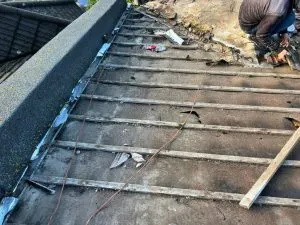 A pitched roof being re-roofed, showing exposed wooden battens and a roofer at work.