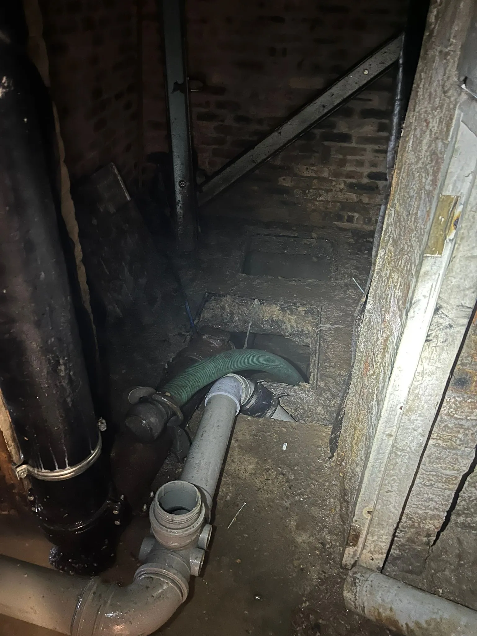 Drainage pipes and hose during cleaning or unblocking in an underground chamber.