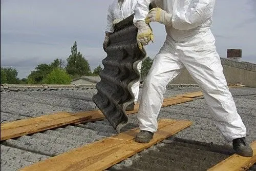 Asbestos removal experts in PPE safely dismantling and removing old corrugated asbestos cement roofing panels.