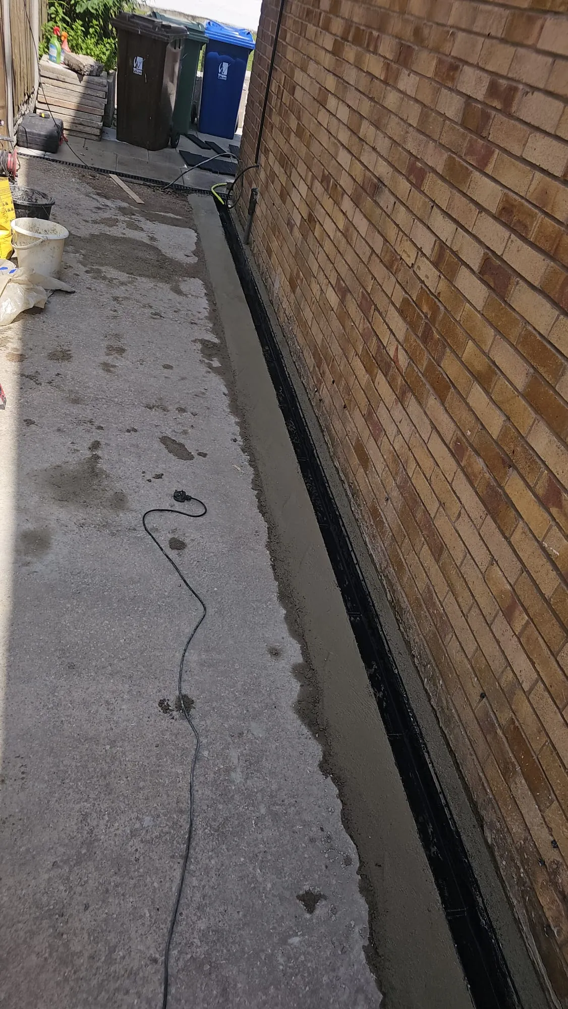 A newly installed linear drain next to a brick wall on a concrete pathway.