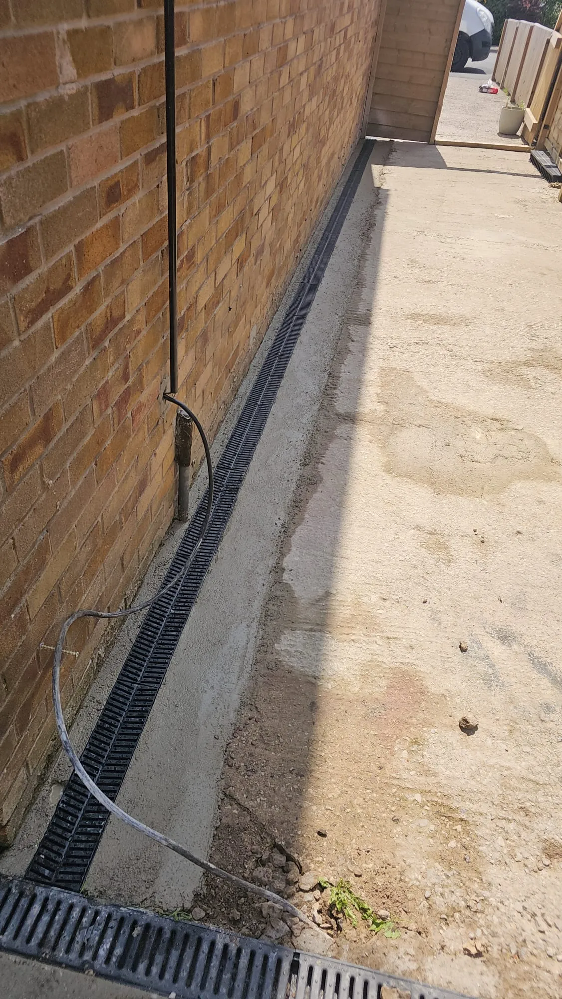 Newly installed linear drainage channel along a brick wall and concrete pathway.