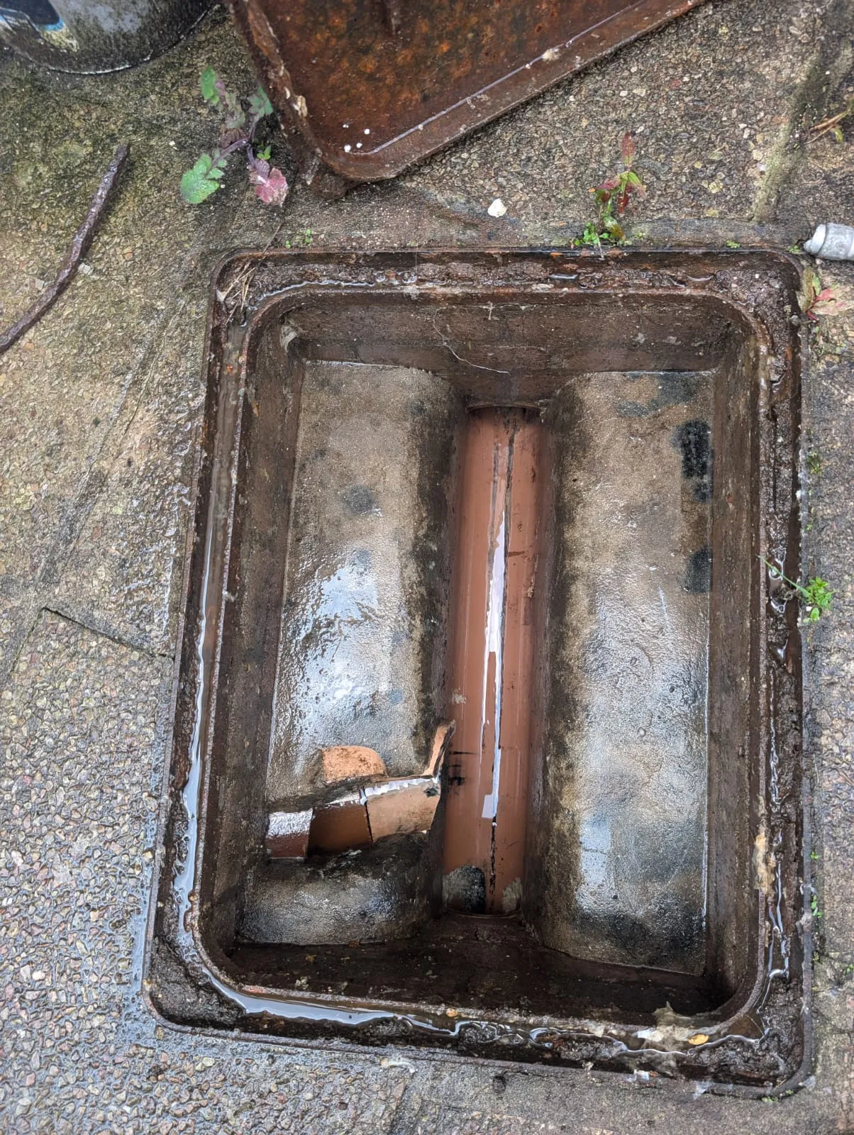 Open drain inspection chamber with standing water and debris