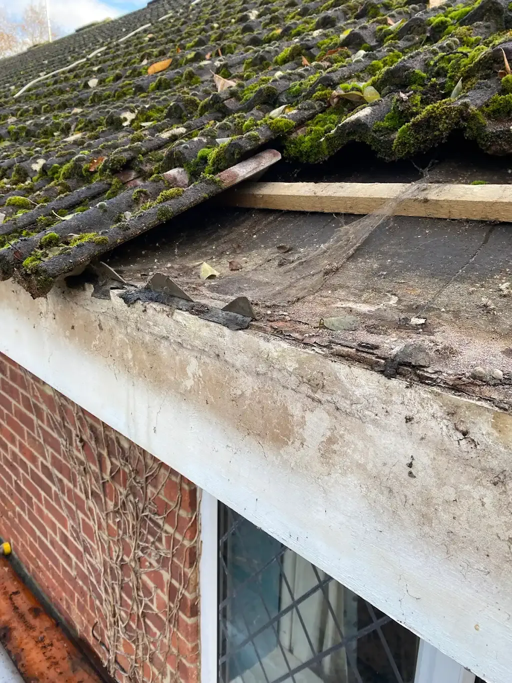 Damaged tiled roof edge with missing tiles and moss