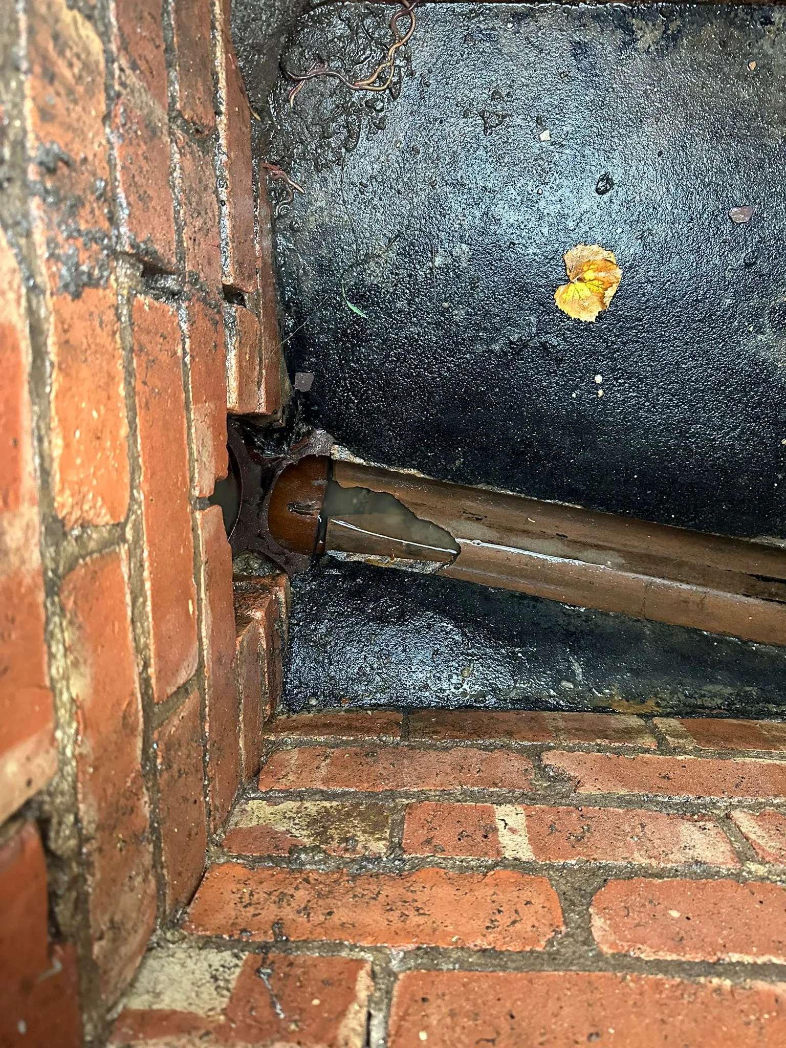 Close-up of a broken drain pipe and pooled water inside a brick inspection chamber, highlighting damage.