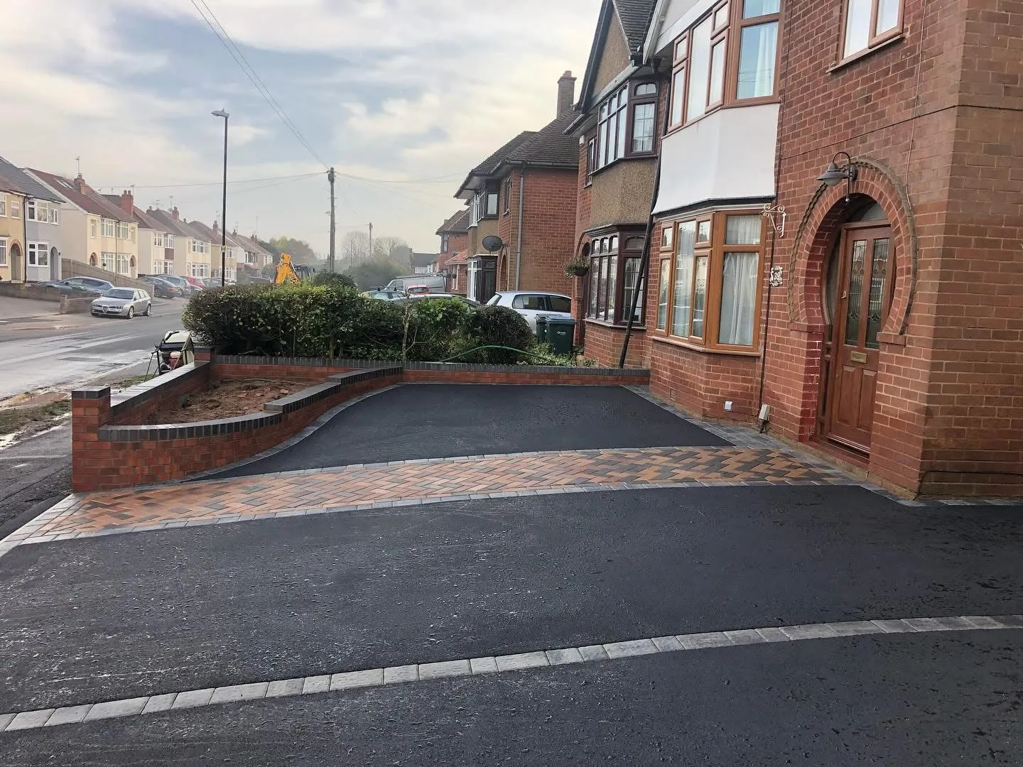 A modern residential driveway featuring a smooth tarmac surface with block paving borders and a curved brick retaining wall.