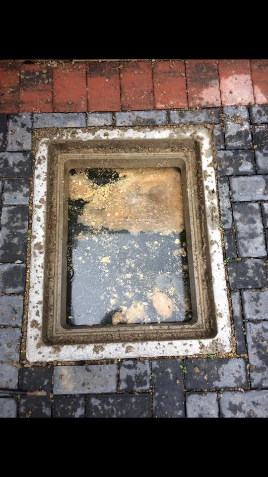 Blocked outdoor gully or manhole with murky water and accumulated debris.