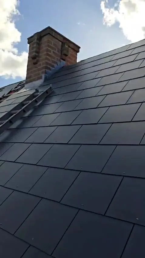 New dark grey tiled roof installation with a brick chimney.