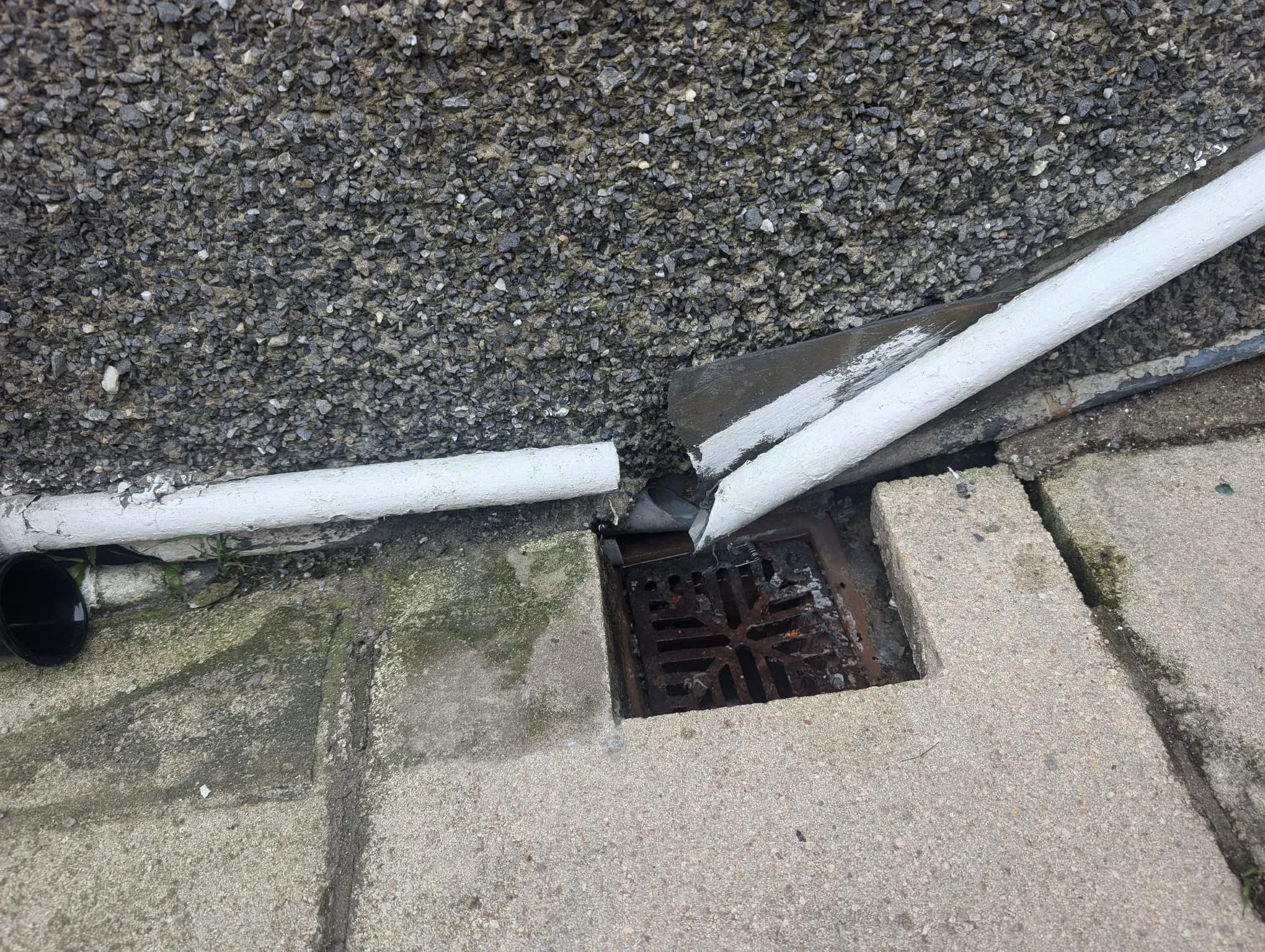 Outdoor drain grate with damaged pipes needing repair.