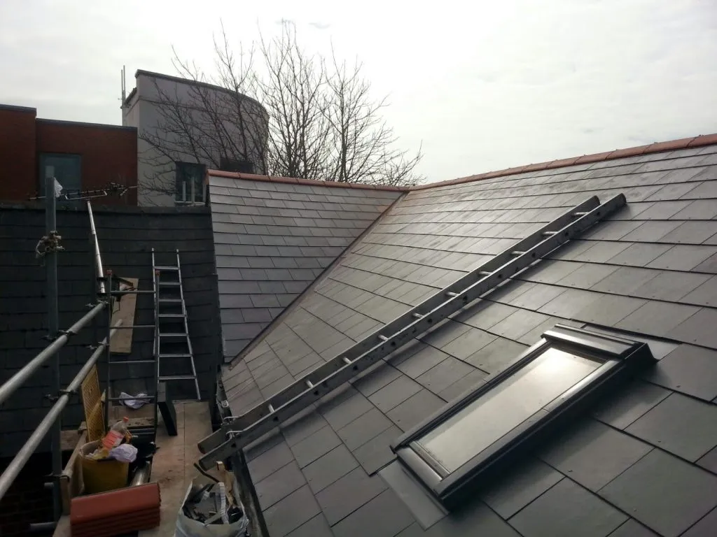 Newly installed dark grey pitched roof with a Velux window, construction ladder, and scaffolding
