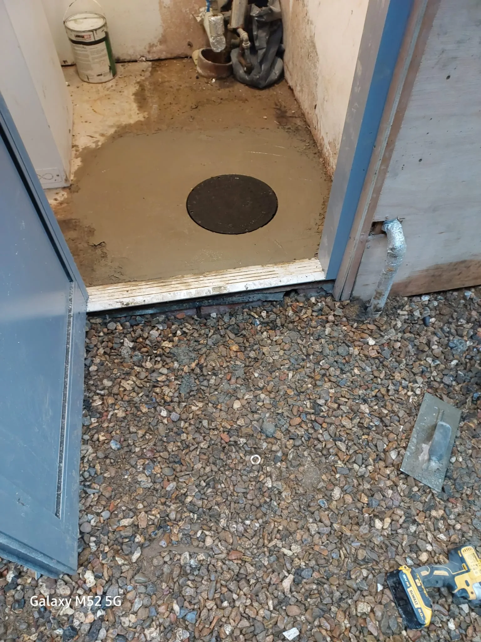 A black drainage manhole cover set into a new concrete floor, indicating access to a septic tank or drainage system for installation or maintenance.