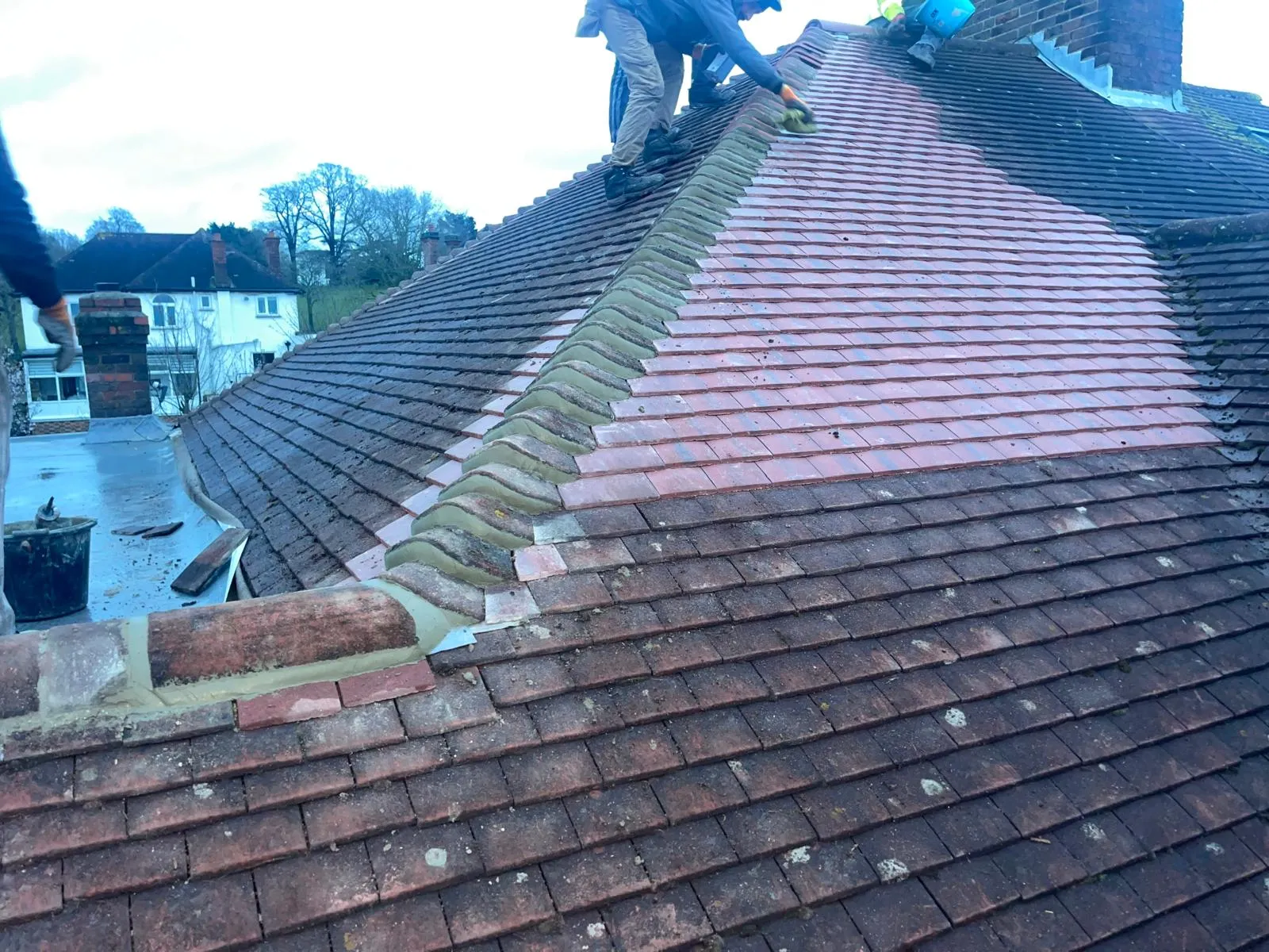 Roofers performing roof cleaning and maintenance on a tiled residential roof.