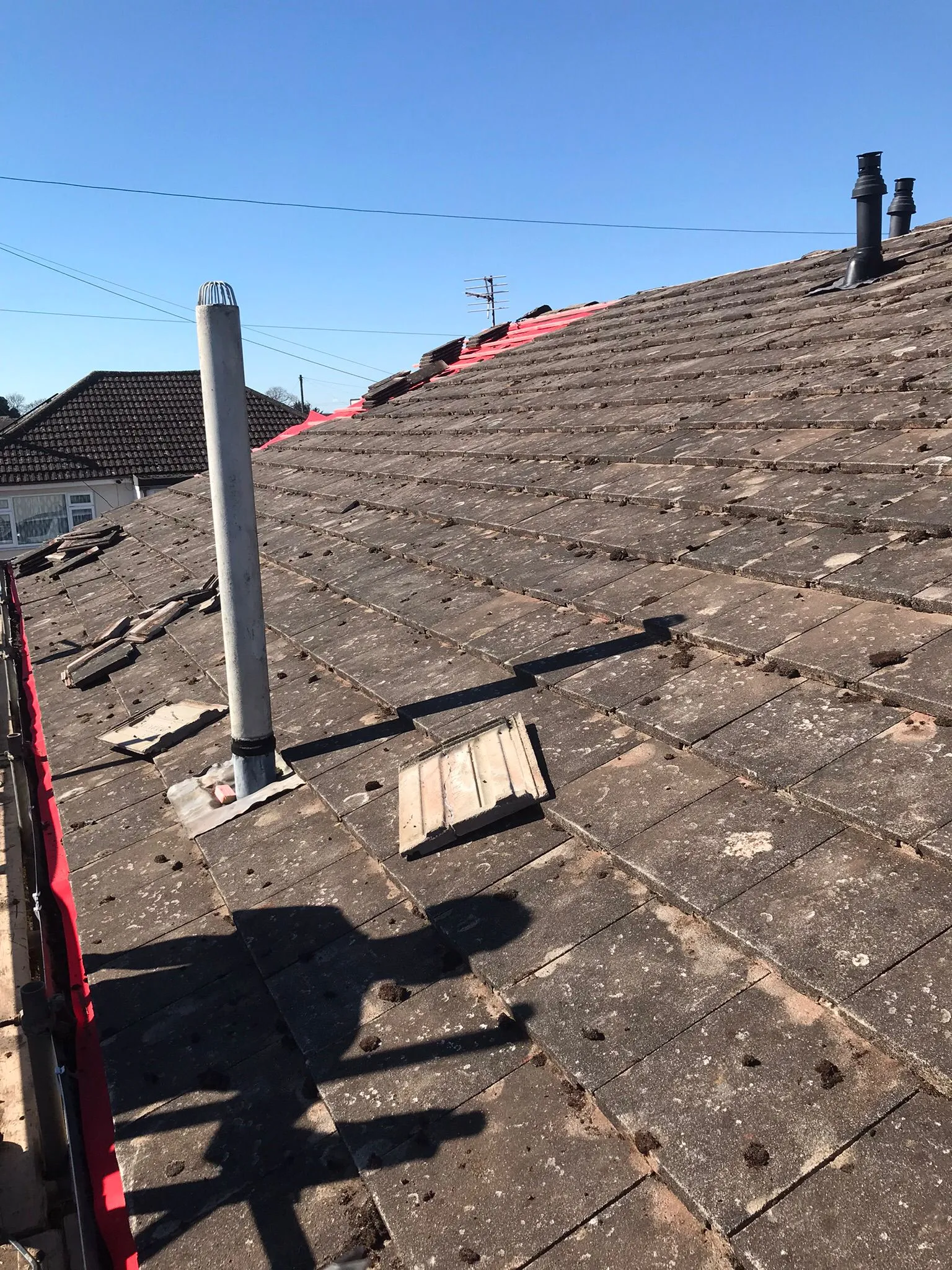 Tiled roof under repair with missing tiles, red underlay, and a large white vent pipe.