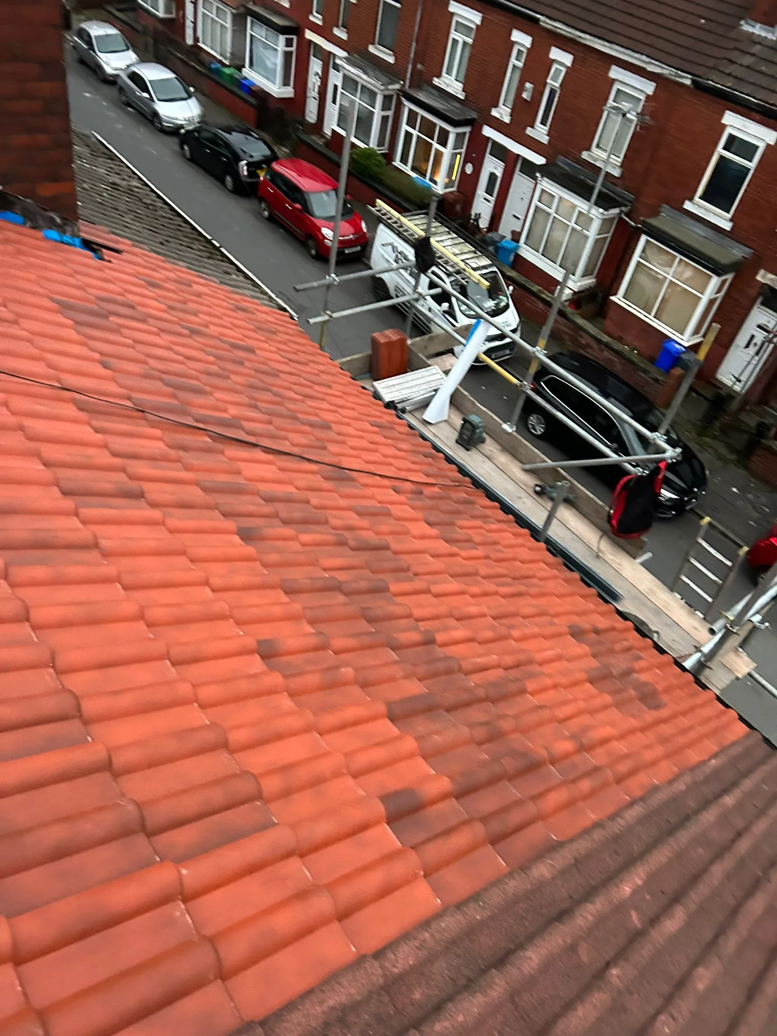 An aerial view of a residential pitched roof with red tiles, some appearing dirty or discoloured, with scaffolding set up for roofing work.