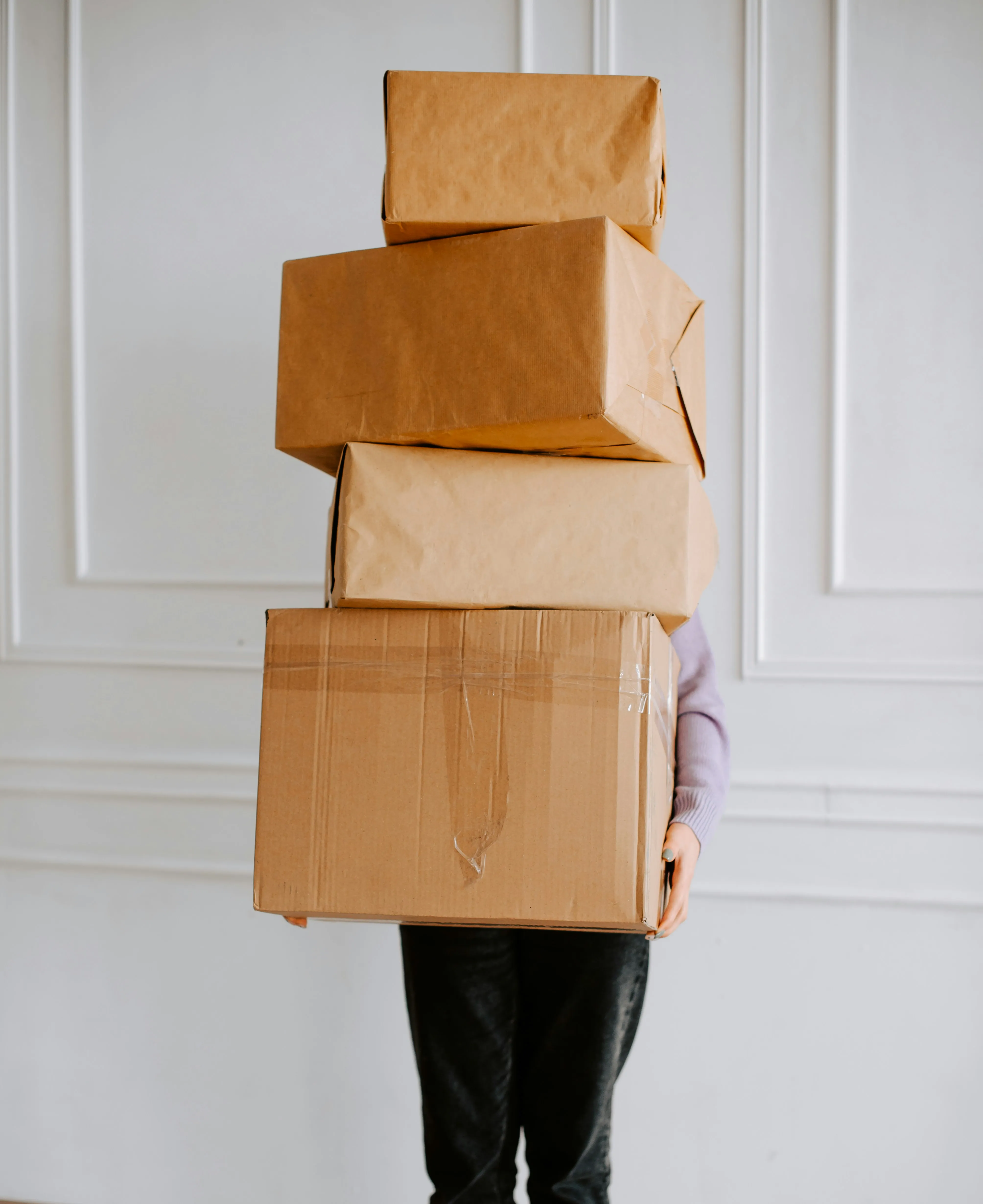 Person carrying a large stack of moving boxes, ready for removal