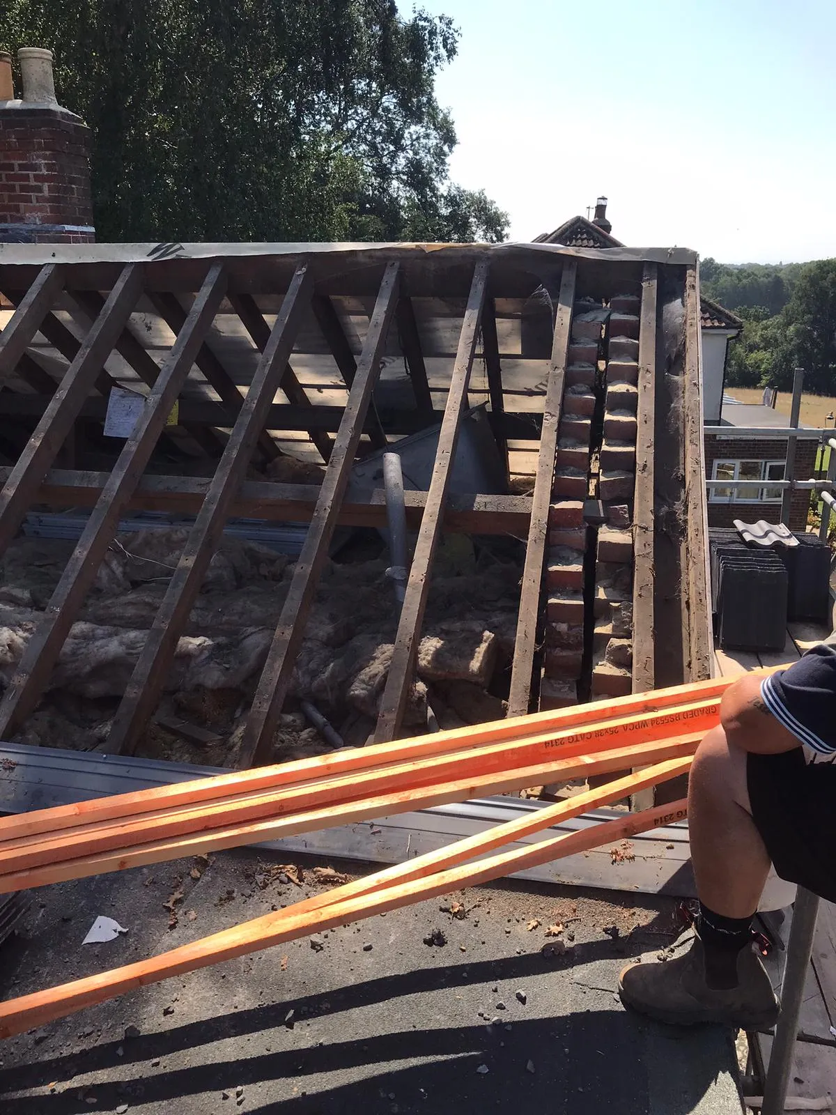 Roof structure under construction with timber rafters, insulation, and building materials.