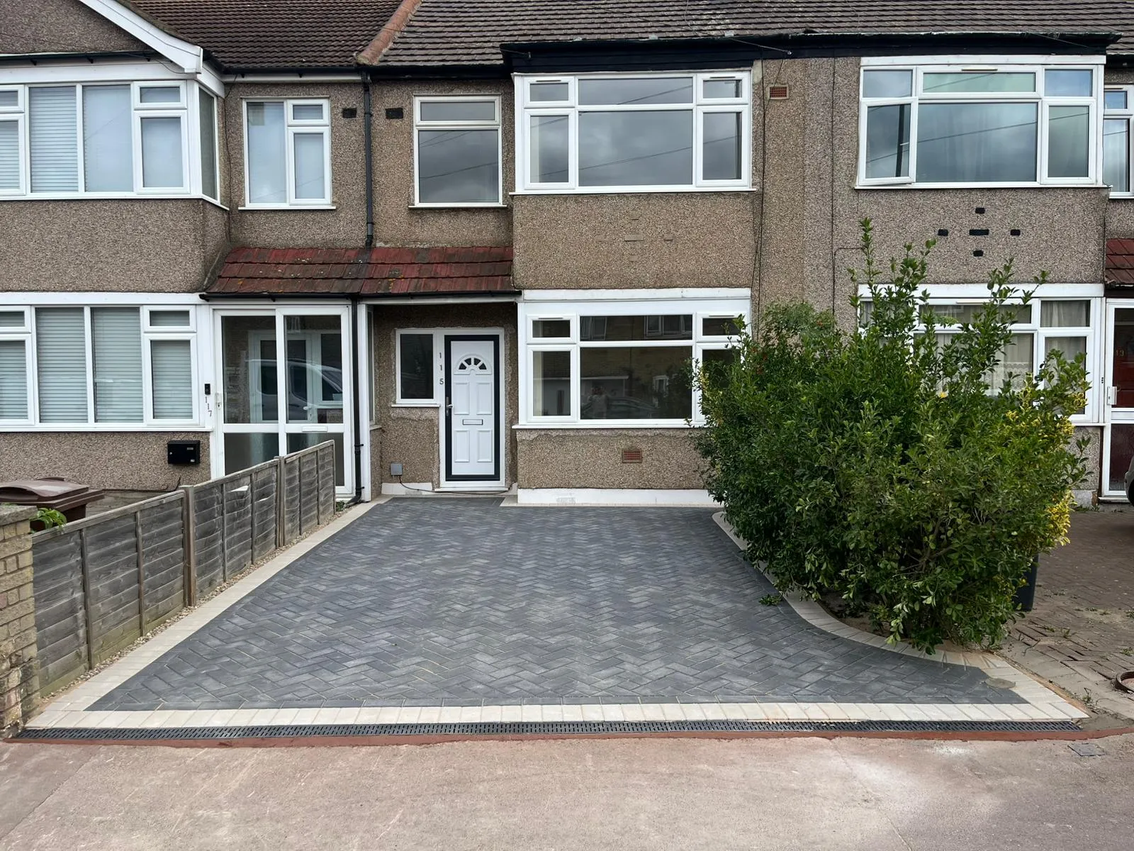 New block paving driveway with dark grey pavers in a herringbone pattern, light grey border, and drainage system in front of a residential property.