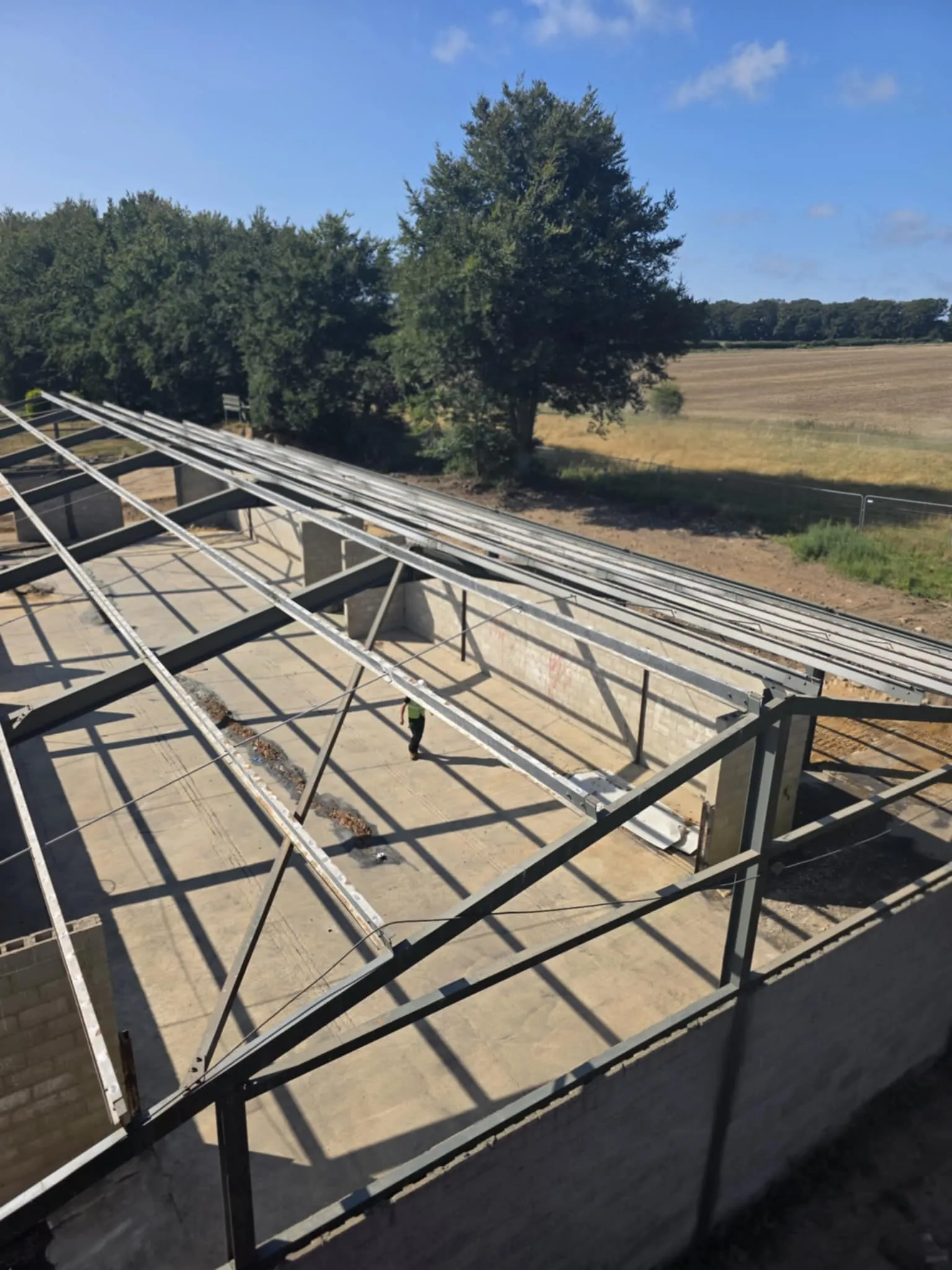 An aerial view of the steel frame of an industrial building, with an individual visible inside, indicating a large-scale asbestos removal or demolition project.