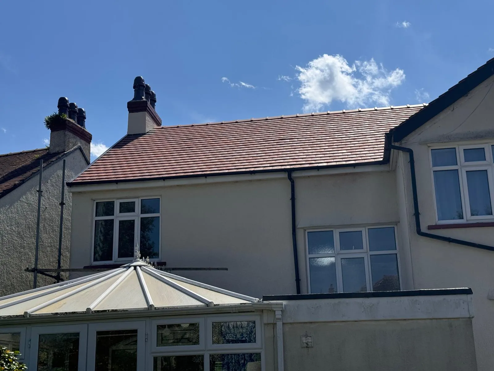 A newly installed red tiled roof on a residential house with chimneys and a conservatory.