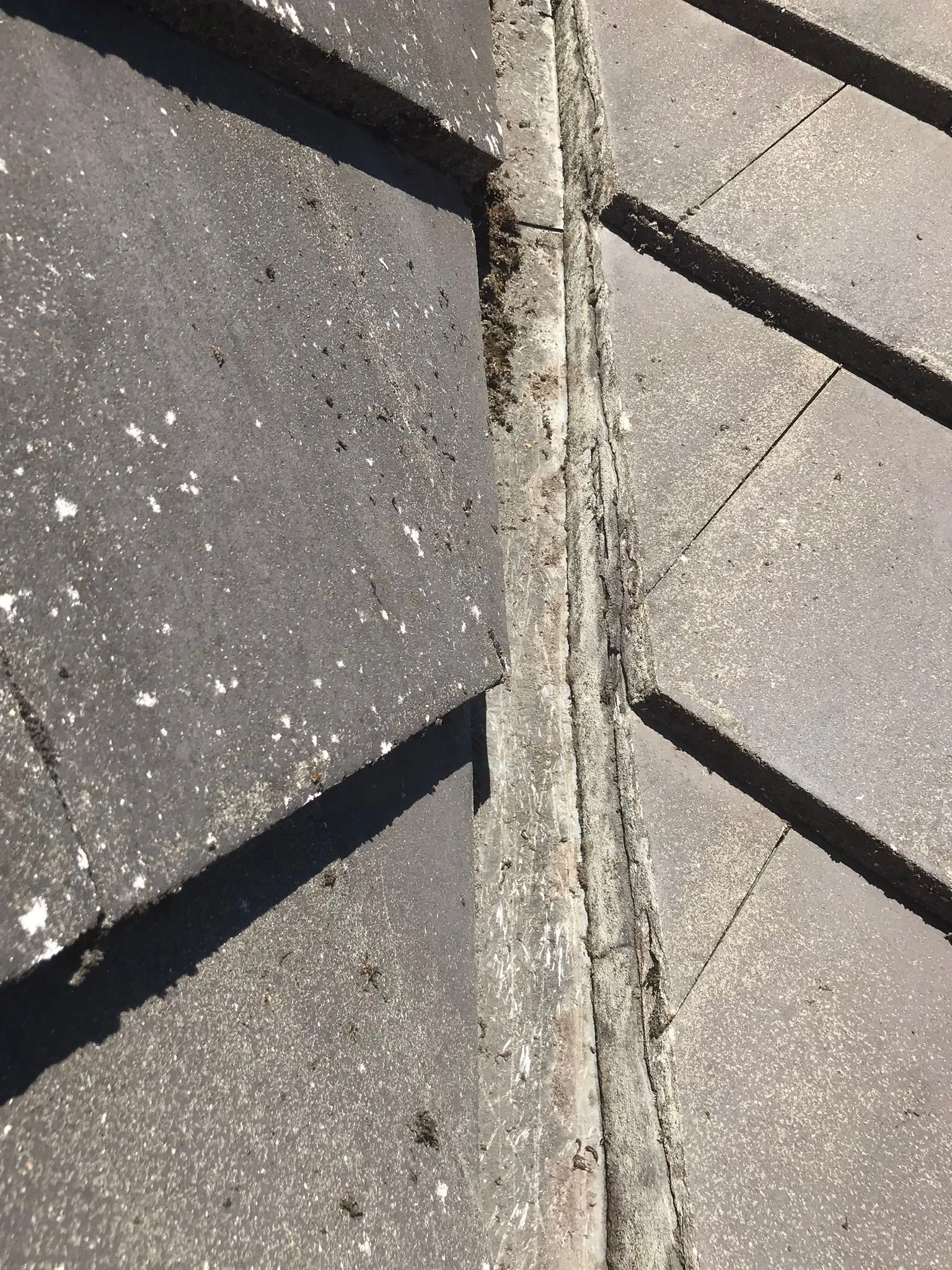 Degraded mortar joint and moss on a residential tiled roof valley.