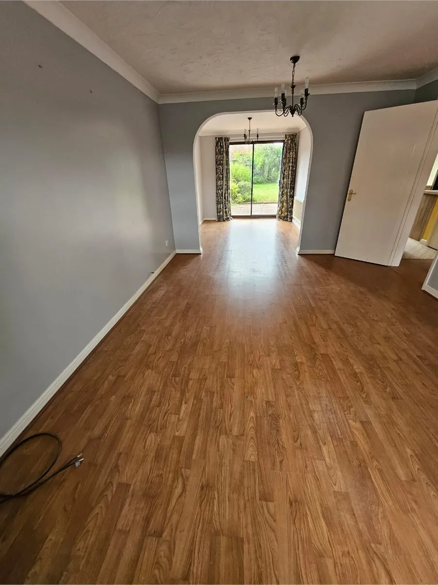 An empty, clean living room with a wooden floor and view to a garden, representing a successfully completed house clearance.