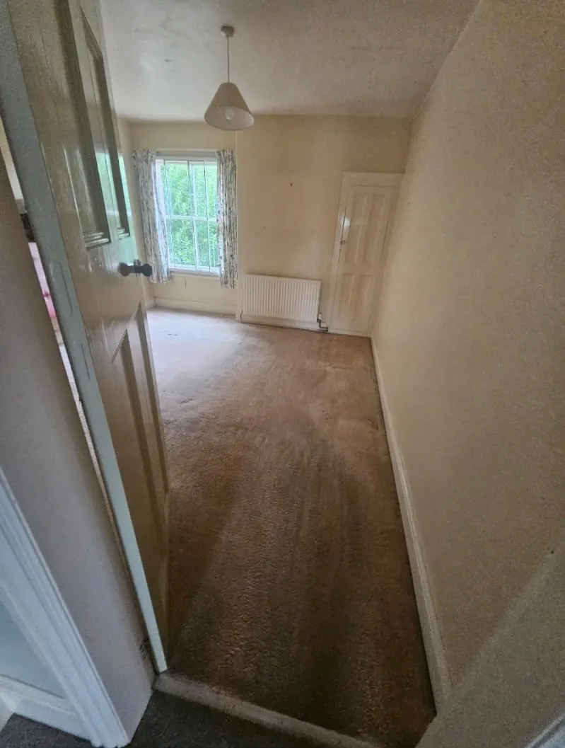 Empty room with brown carpet, light walls, window, and radiator after a house clearance or end-of-tenancy service by Llandudno Rhos on sea House Clearance.