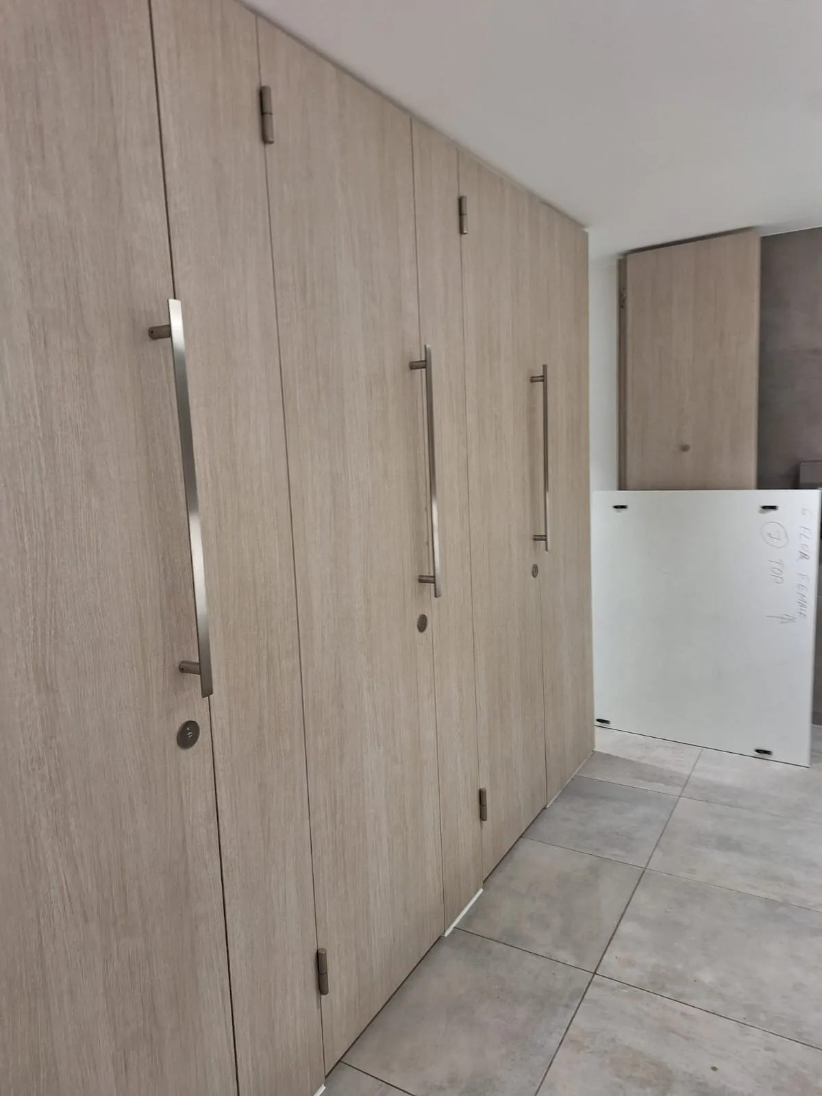 Modern commercial washroom cubicle doors or changing room lockers with metal handles, representing a commercial property serviced by drainage professionals.