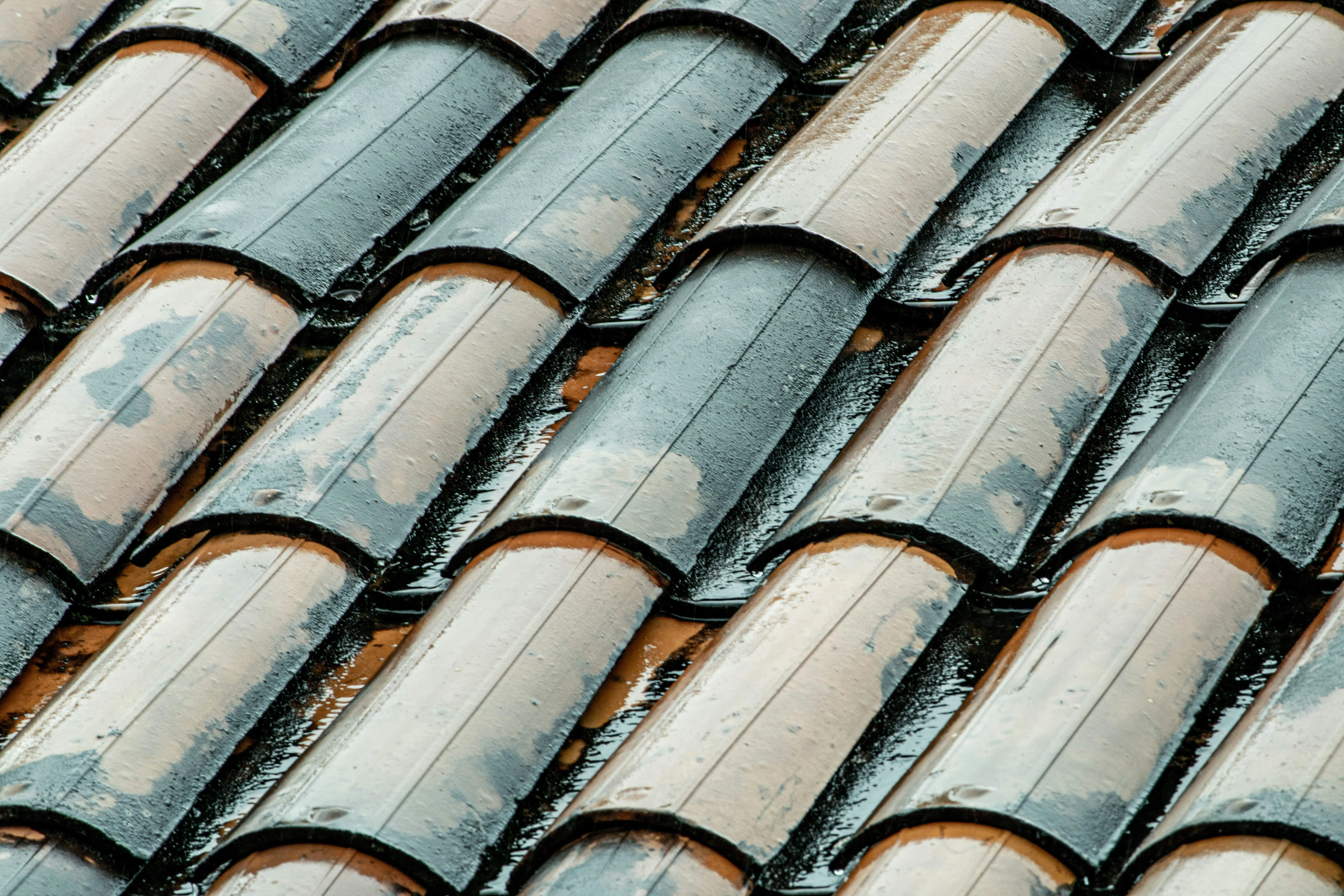 Close-up of traditional terracotta clay roof tiles wet with rain, highlighting their curved shape and overlapping pattern, typical of pitched roofs.
