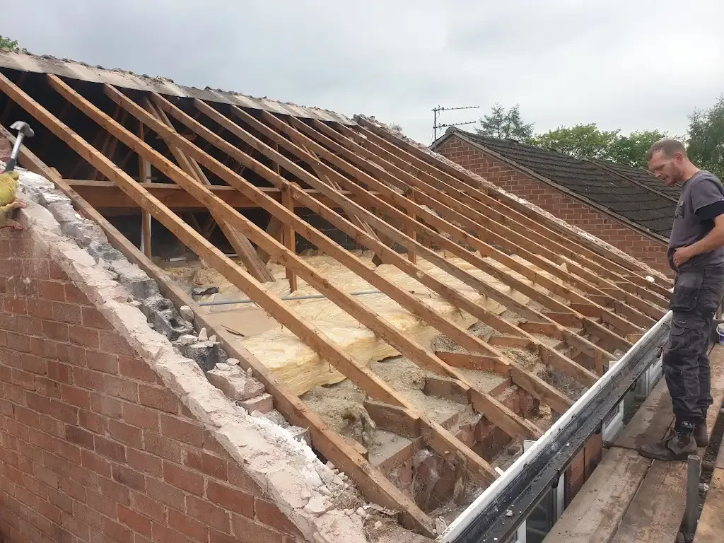 Two roofers undertaking roof repair or replacement, showing exposed wooden rafters and insulation.