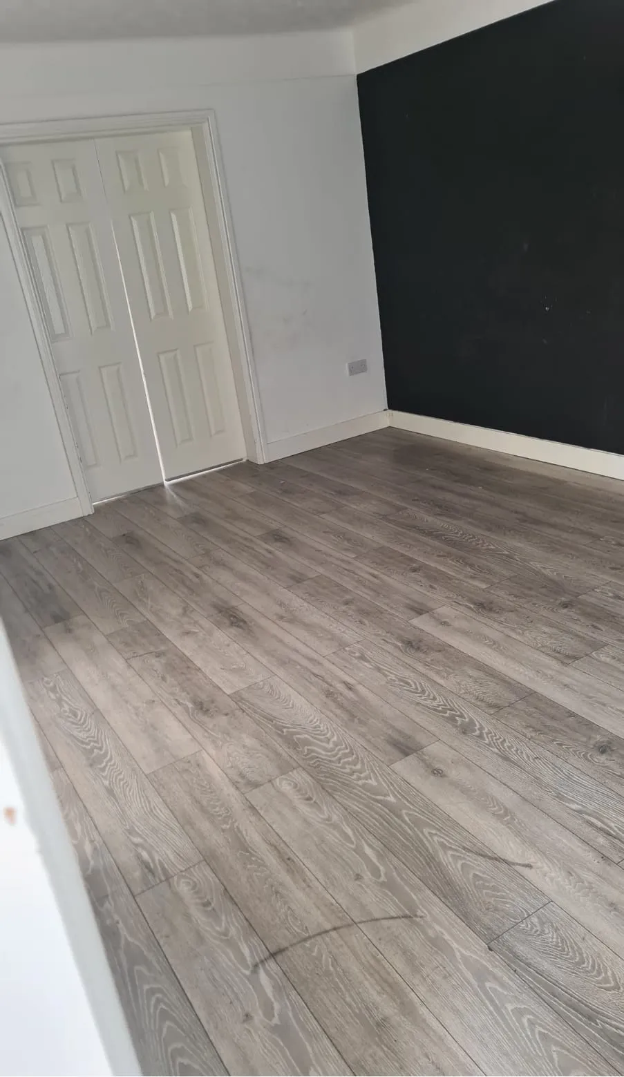 Clean, empty room with laminate flooring and dark accent wall after an end-of-tenancy or house clearance in Llandudno