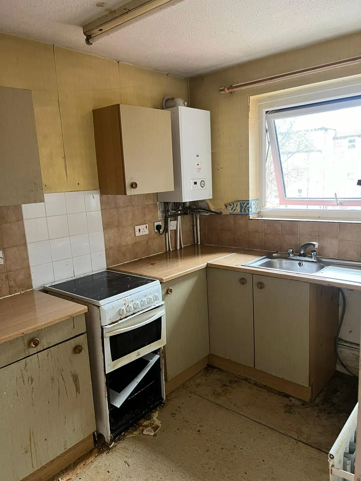 A severely neglected kitchen with damaged cabinets and a broken oven, ready for a full strip-out and waste removal.