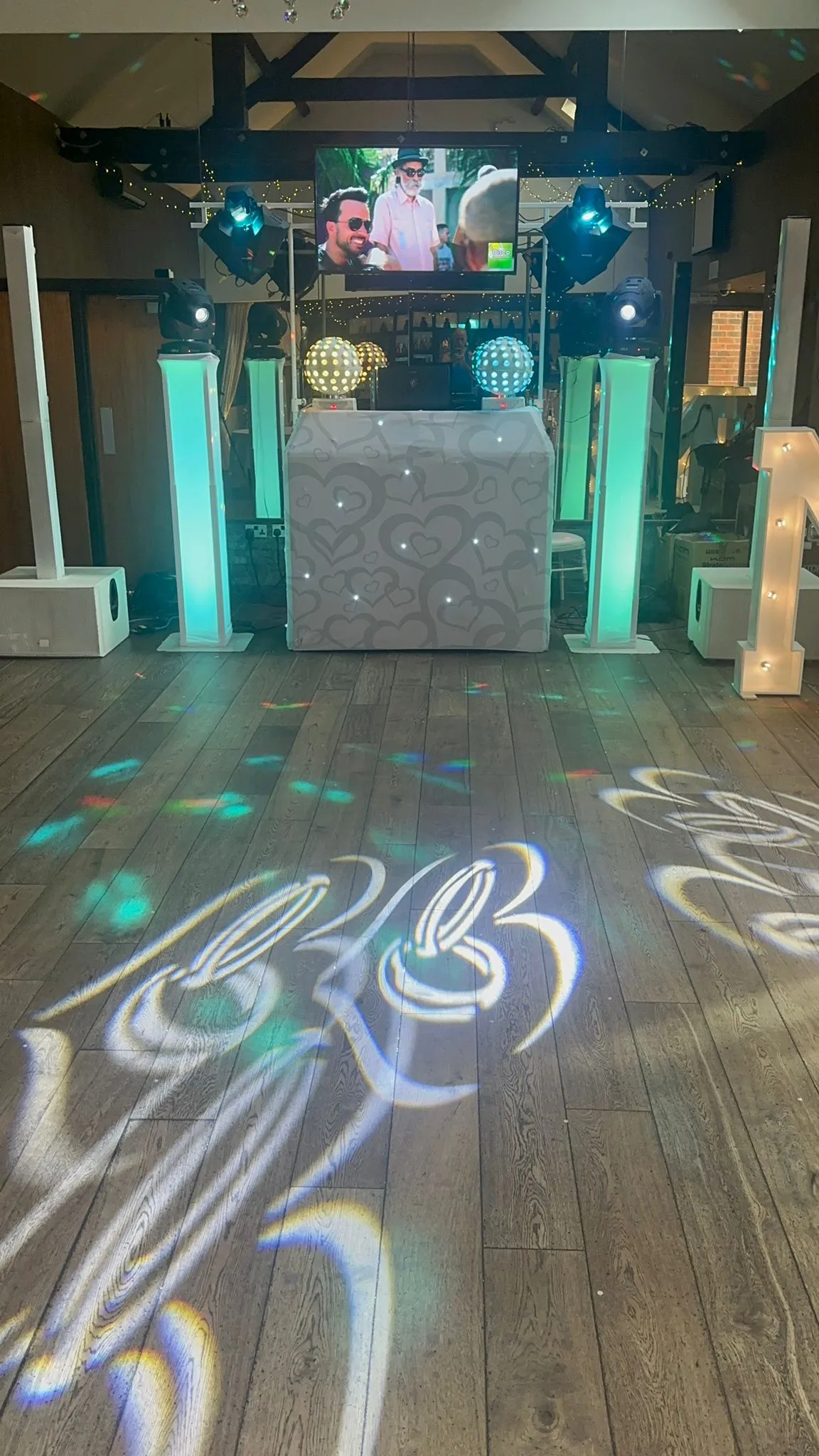 Professional DJ setup from Disco Entertainers with a white illuminated booth, large screens, dynamic lighting, and sound system, ready for an event.