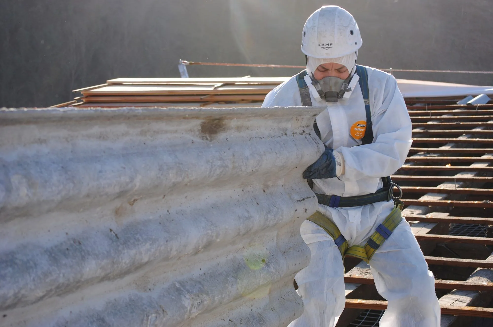 Expert in full PPE safely removing a corrugated asbestos roof sheet.
