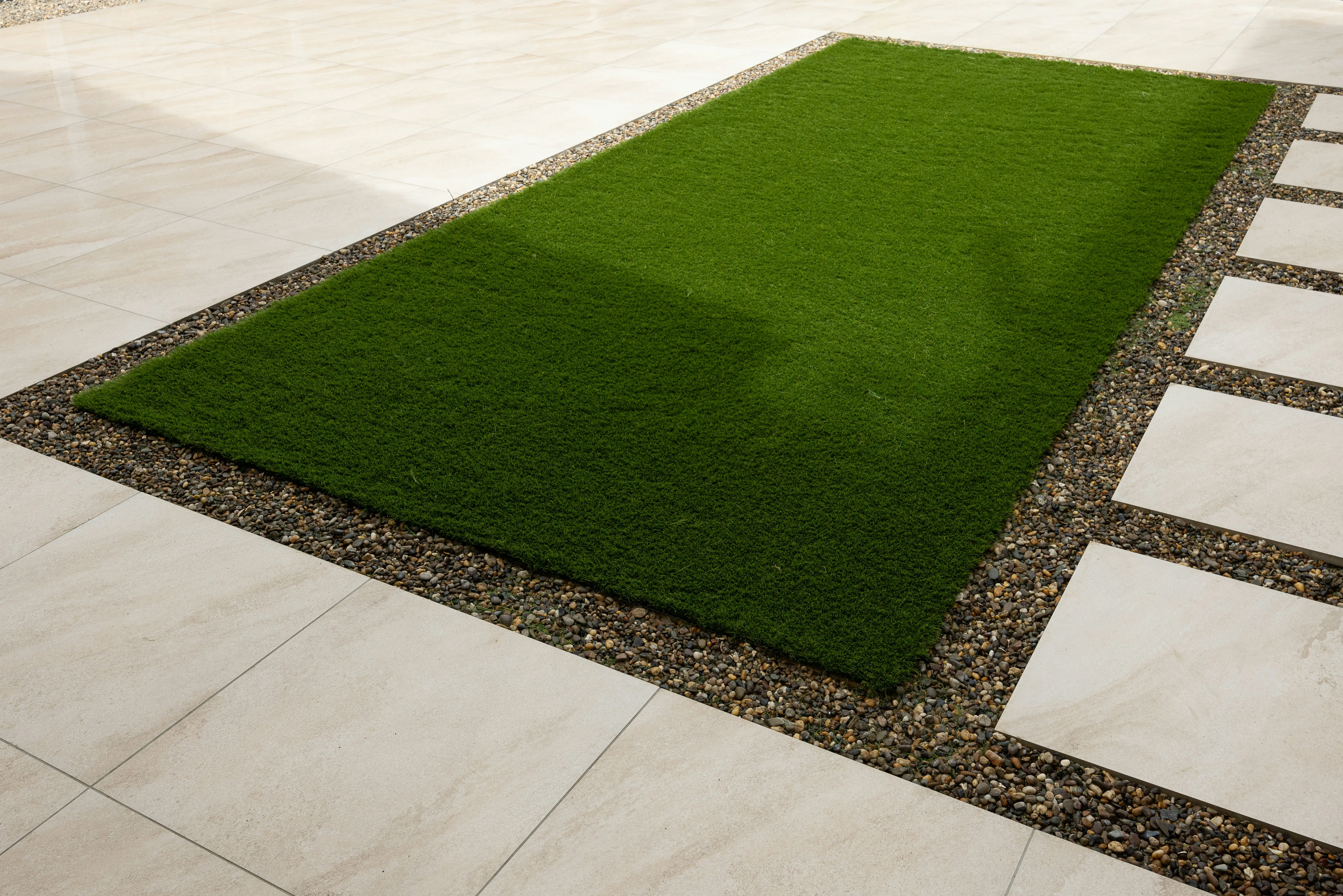 Modern patio with light paving slabs, artificial grass, and gravel with stepping stones.