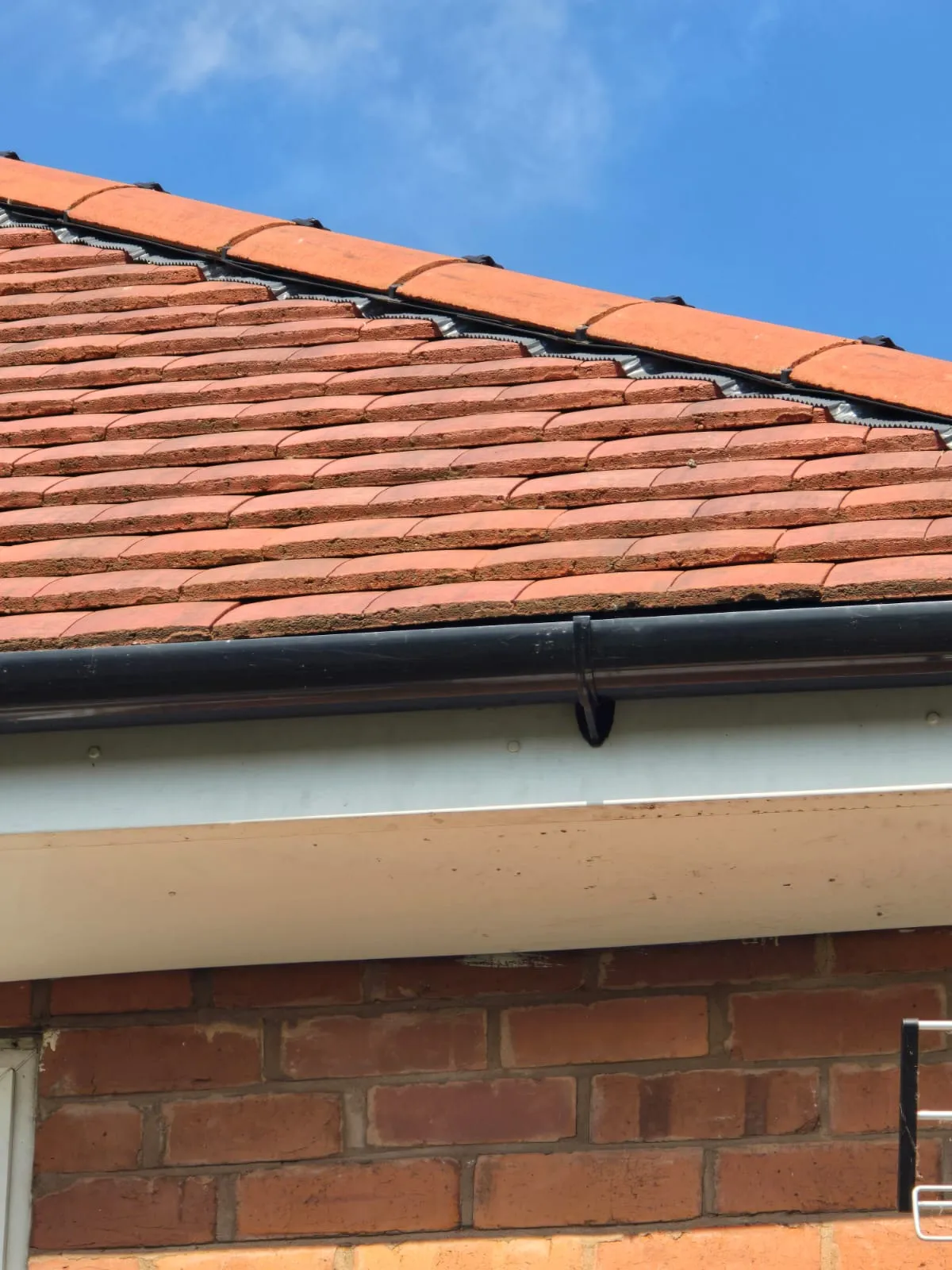 Modern residential roofline with terracotta tiles, dry verge system, black uPVC gutter, and white uPVC fascia.