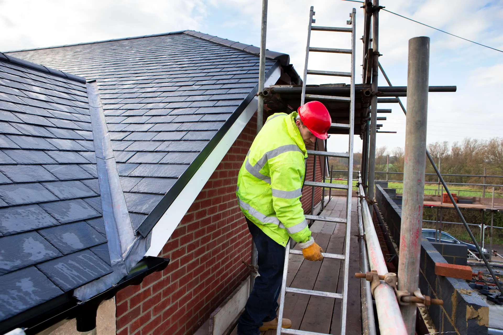 Roofer on scaffolding working close to tiled roof structure on a modern building