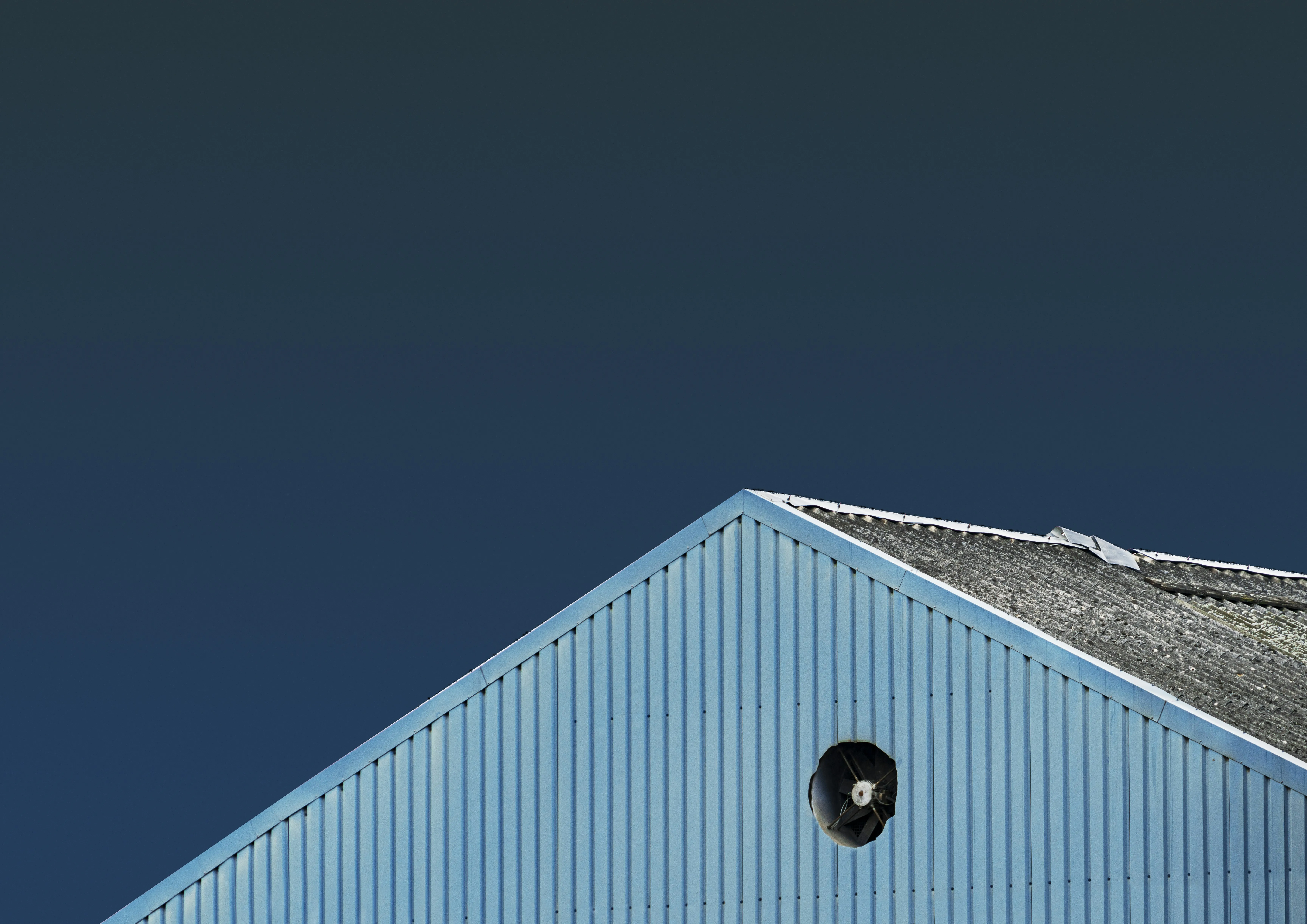 Weathered corrugated roof and light blue metal siding on a building, under a dark blue sky.