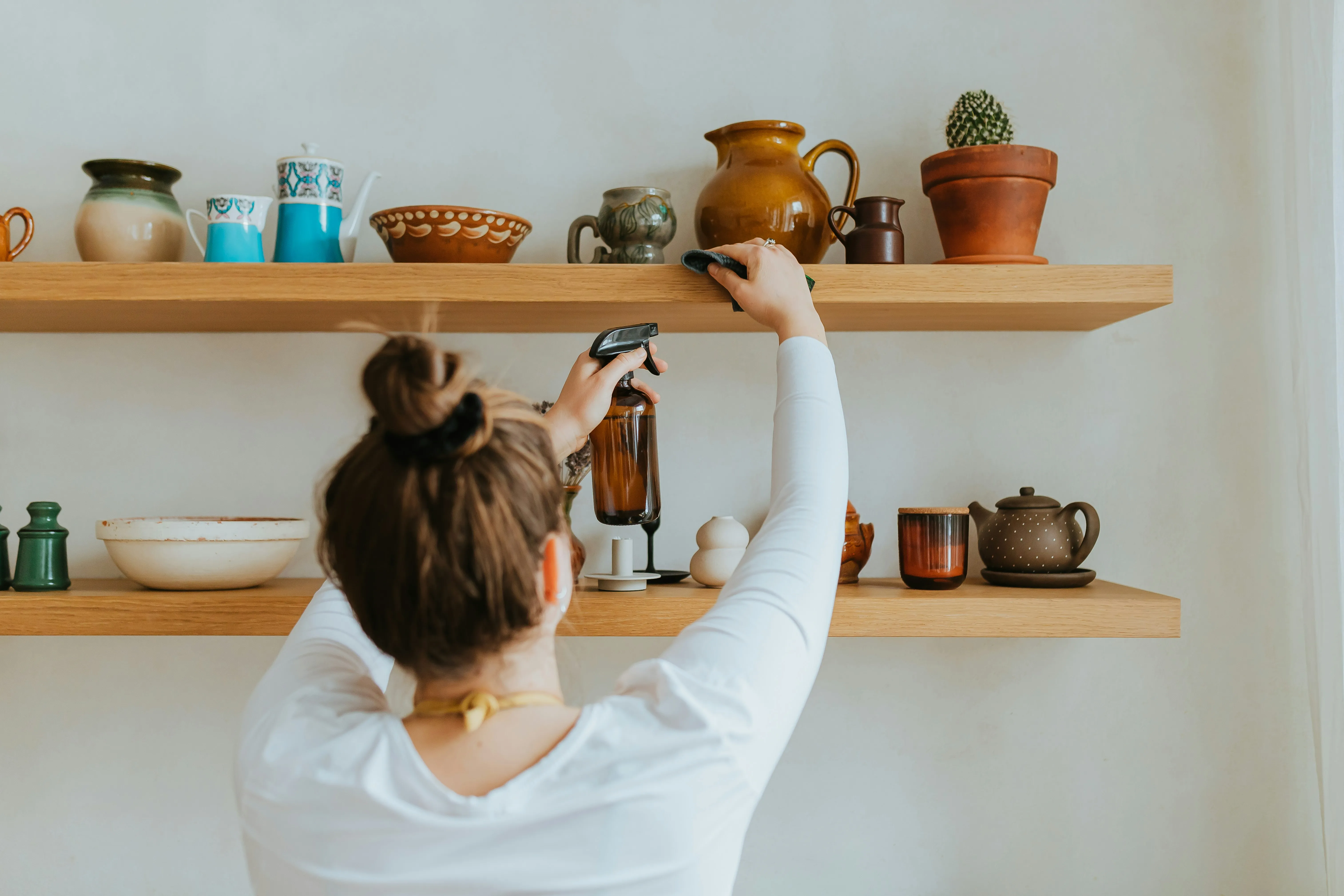 A professional cleaner meticulously wiping shelves and ornaments with a spray bottle and cloth.