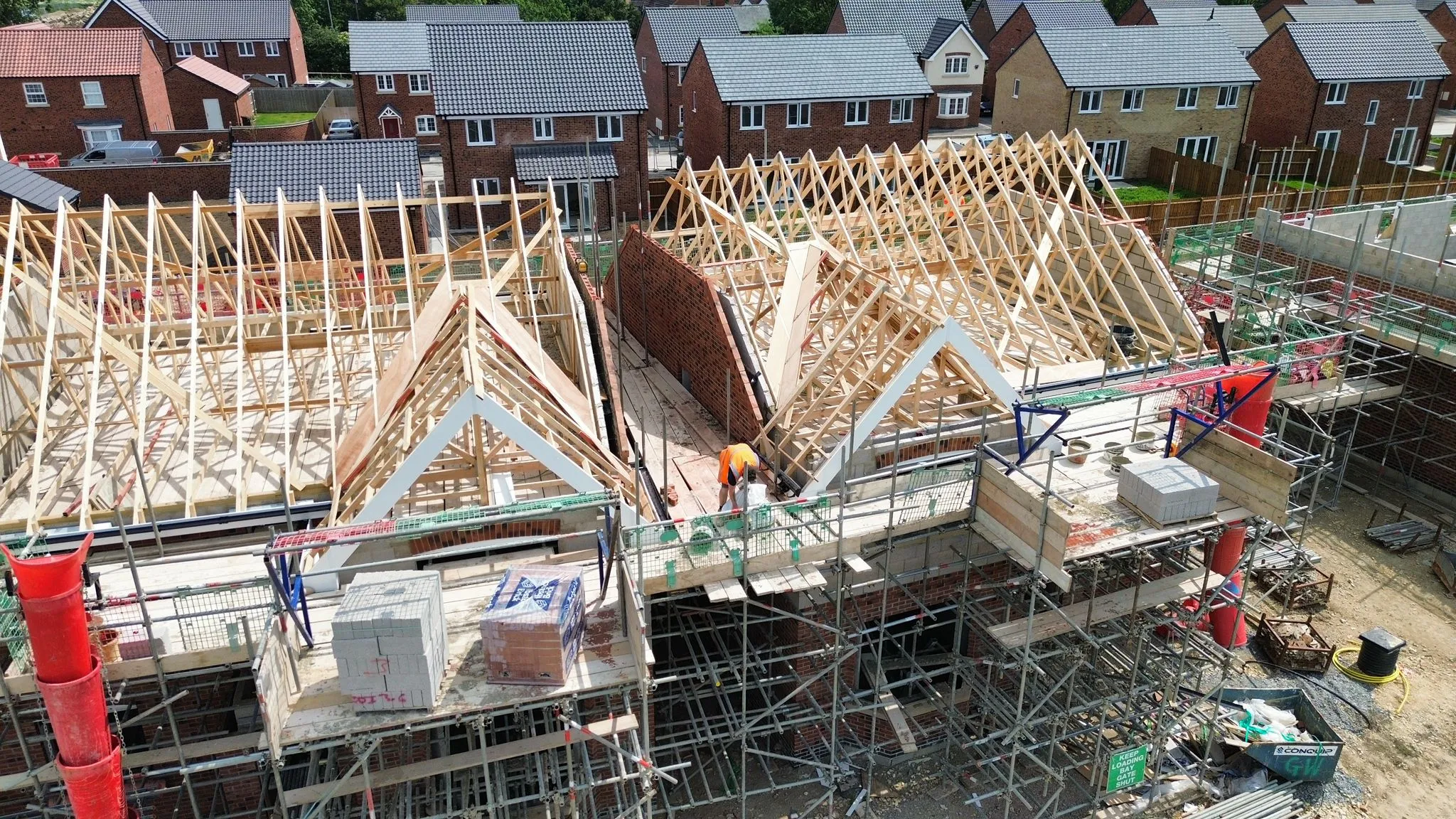 Drone view of new build houses under construction, showing exposed timber roof trusses and scaffolding, illustrating new roof installation in progress by Foster and Son.