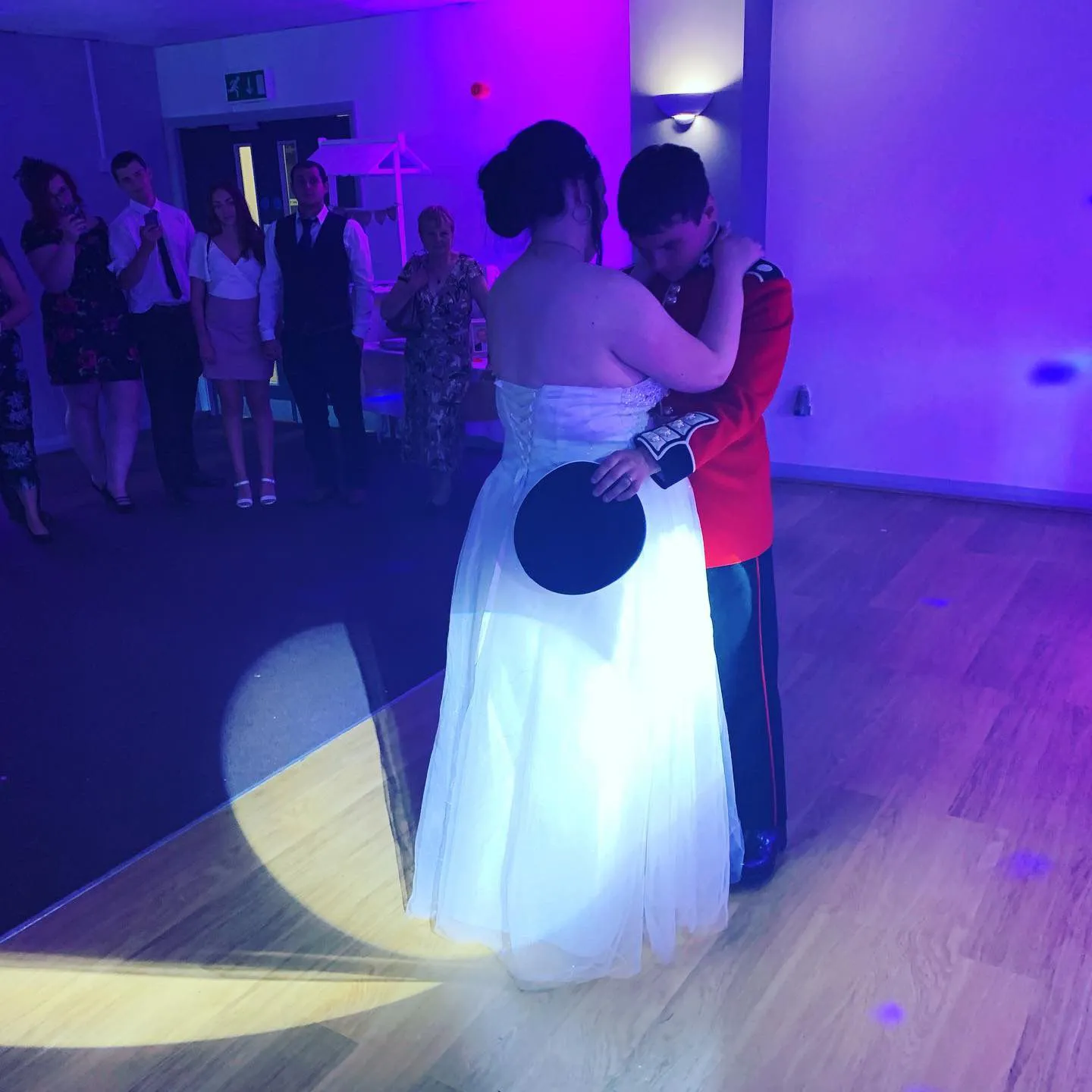 A wedding couple dances under purple ambient lighting and a spotlight, capturing a magical first dance moment at their reception.