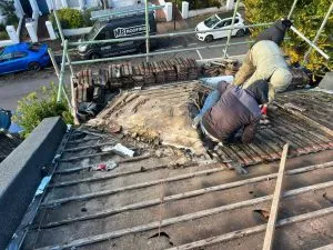 Roofers on scaffolding removing old tiles from a pitched roof, preparing for a new roof installation.